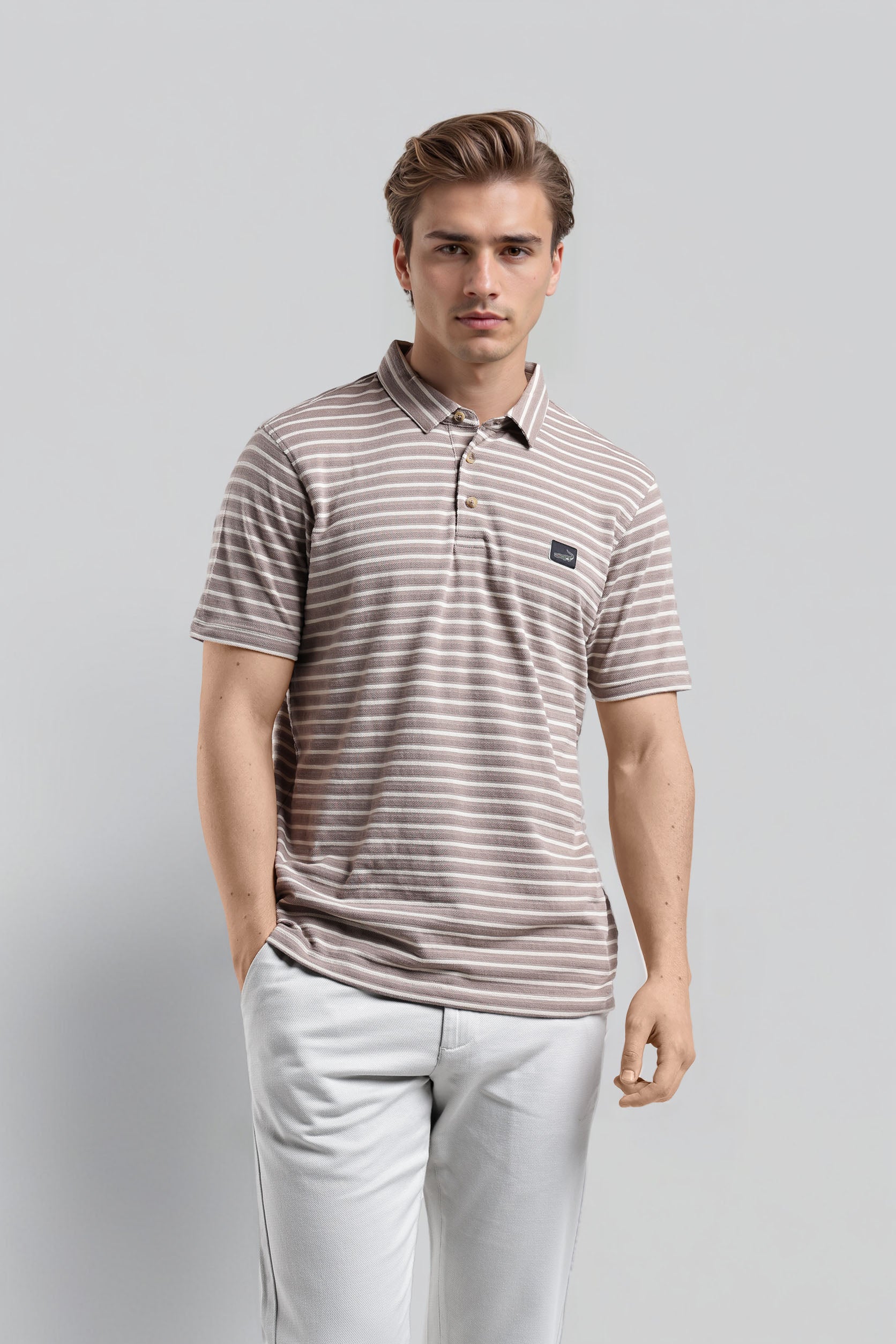 Man wearing a striped polo shirt and light pants on a gray background