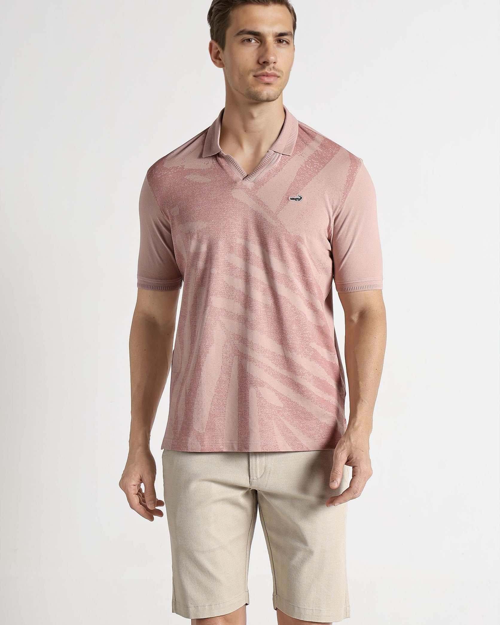 Man wearing a pink polo shirt and beige shorts on a white background