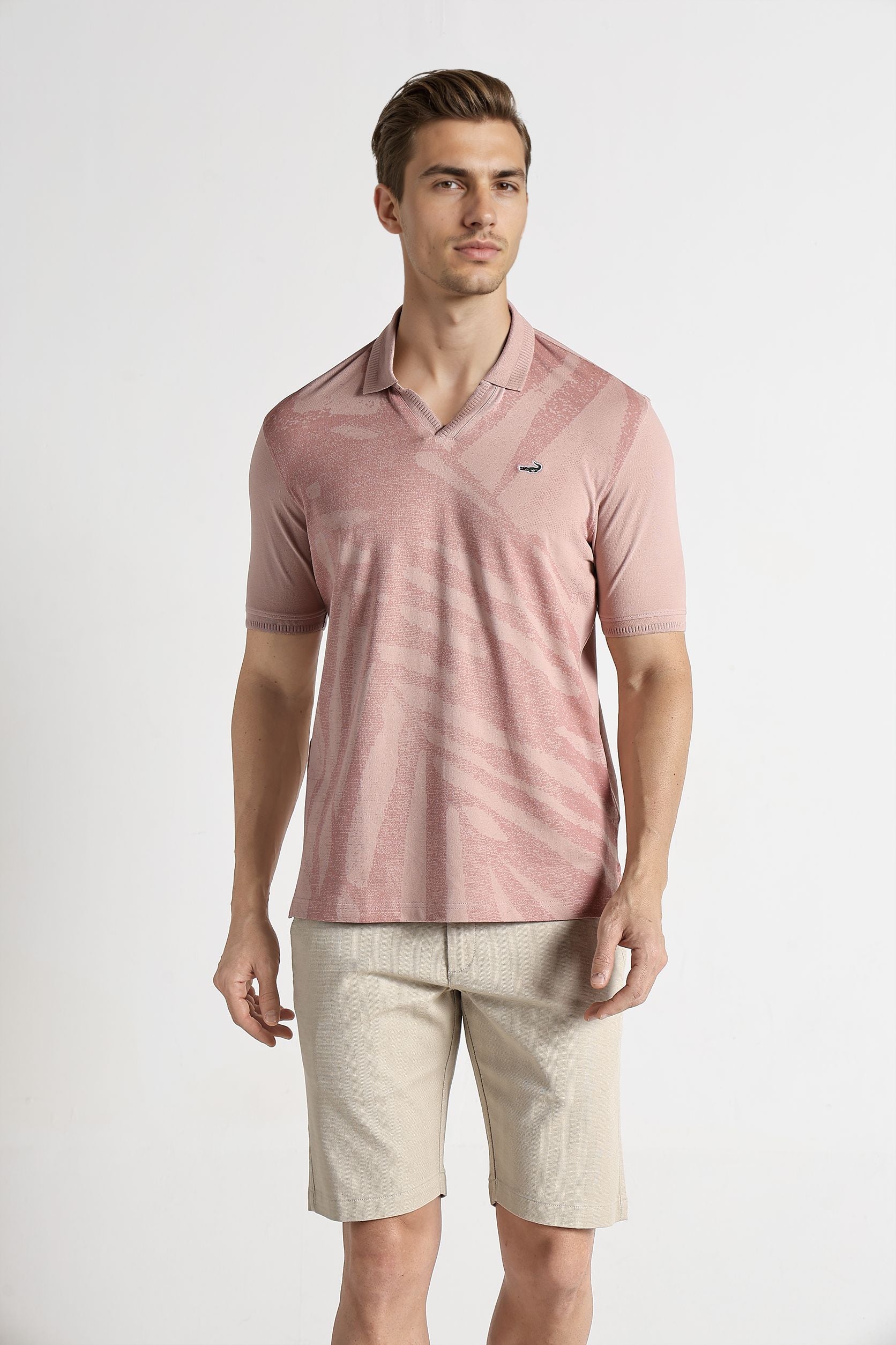 Man wearing a pink polo shirt and beige shorts on a white background