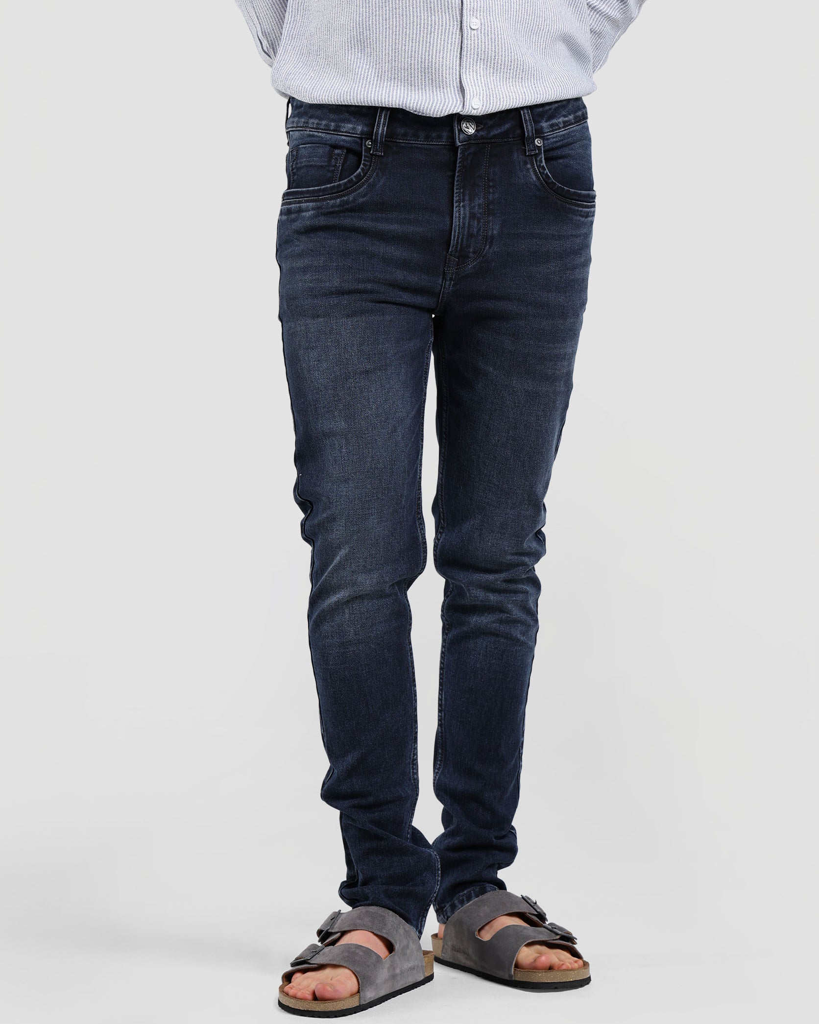 Person wearing dark jeans and sandals on a plain background