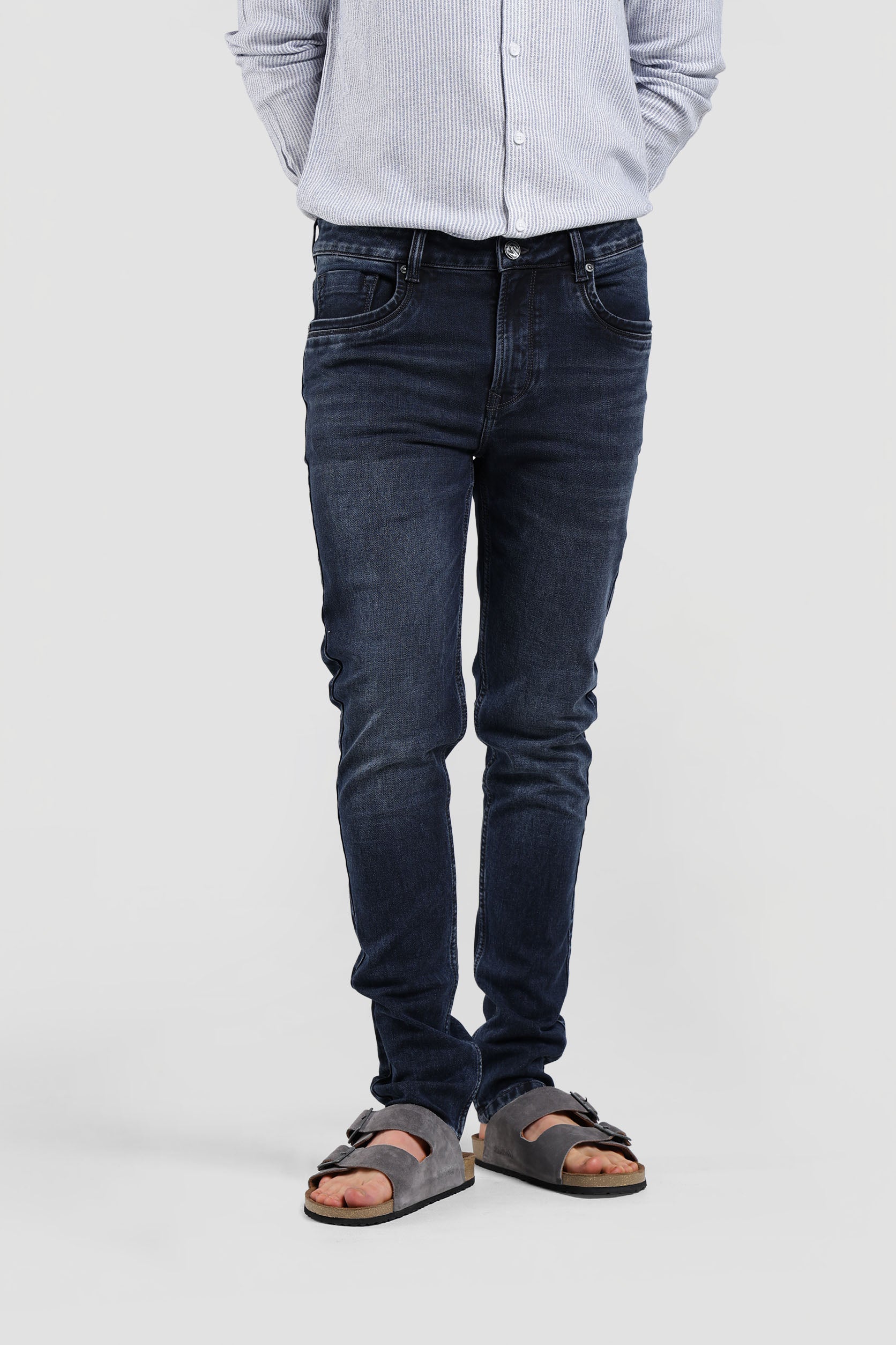 Person wearing dark jeans and sandals on a plain background