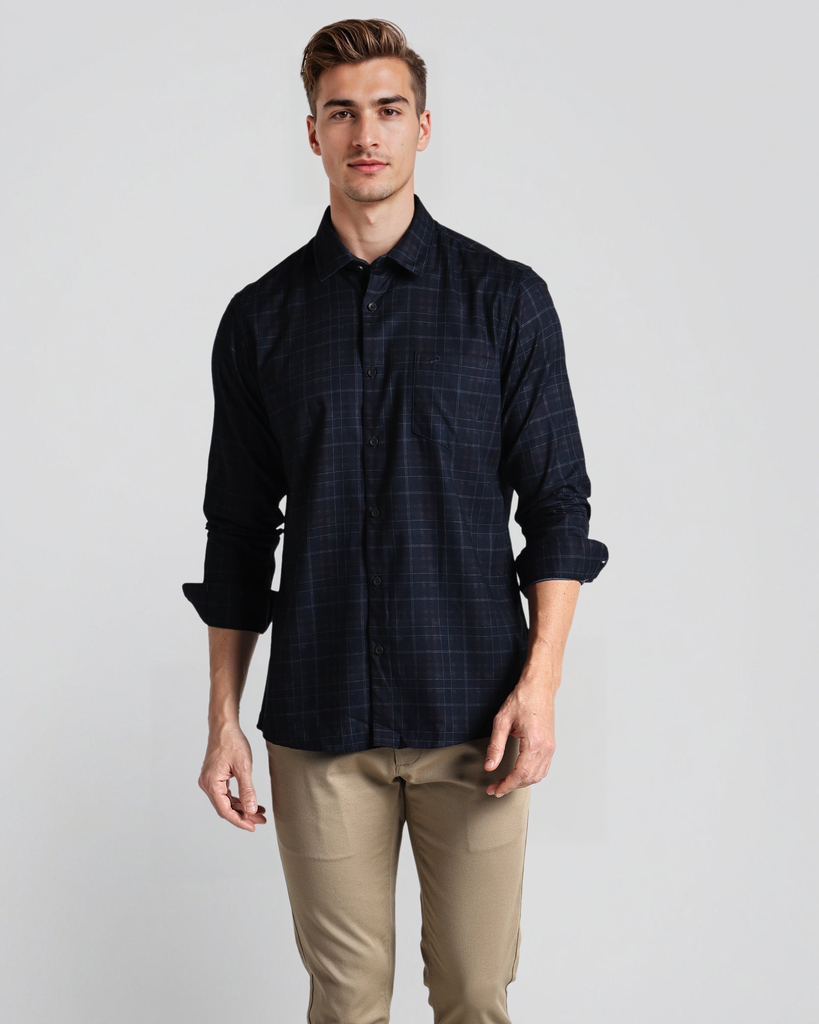 Man wearing a dark plaid shirt and beige pants against a plain background