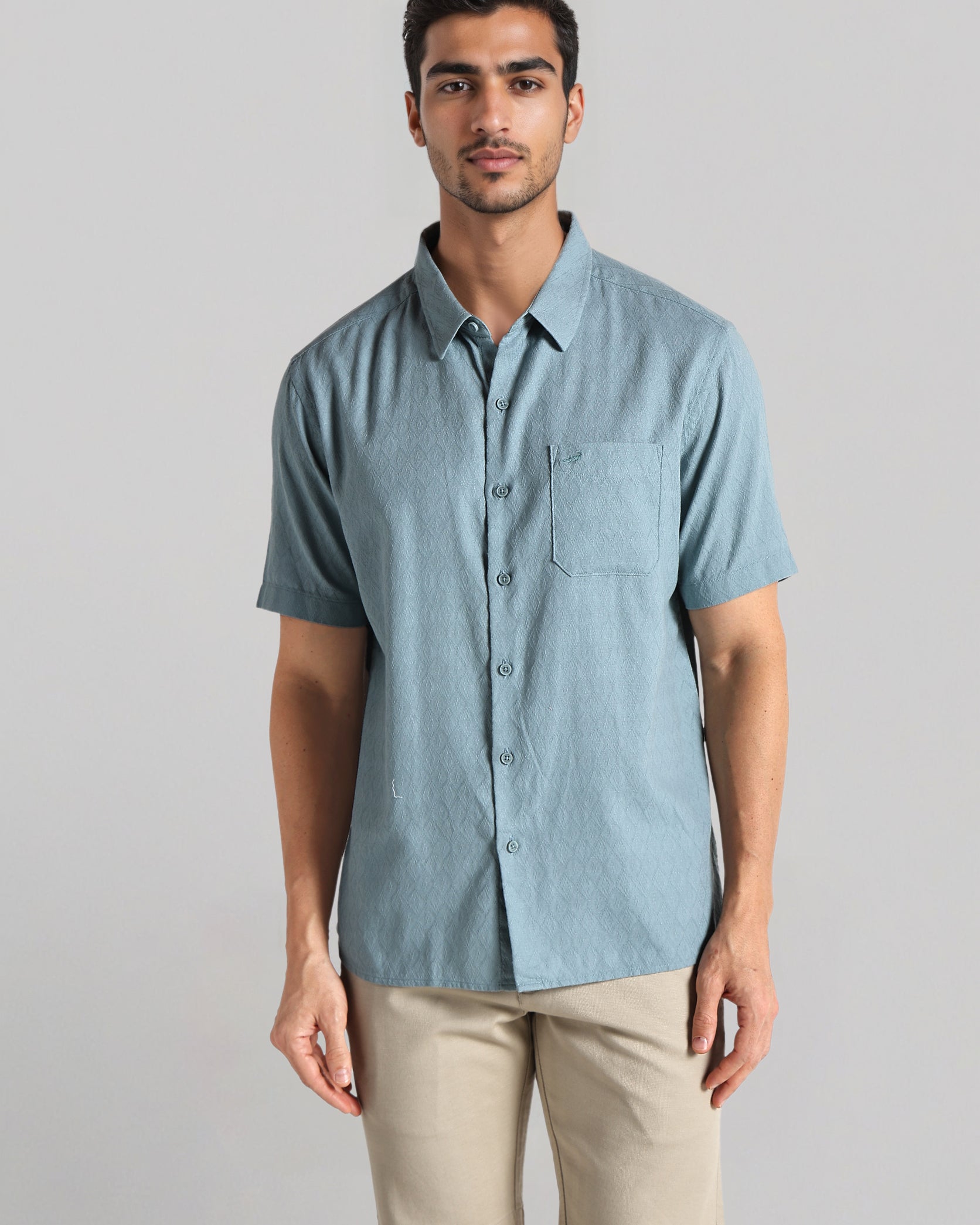 Man wearing a light blue button-up shirt and beige shorts on a gray background