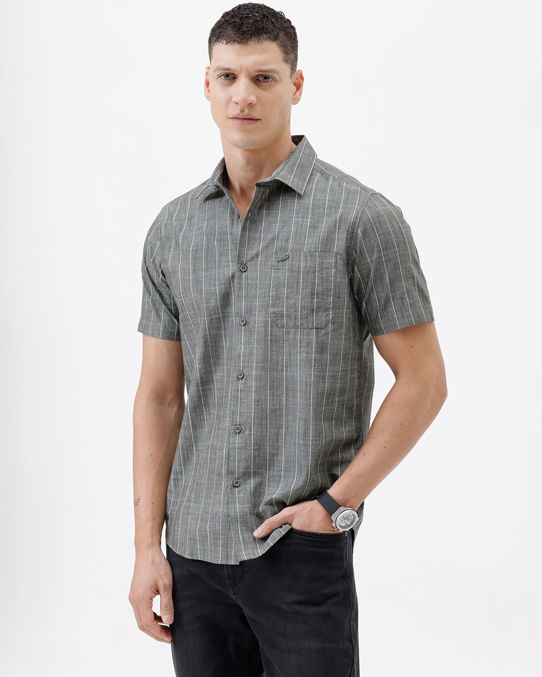 A man wearing a short-sleeve button-up shirt with a gray and white vertical stripe pattern, paired with black pants, standing against a plain white studio background.