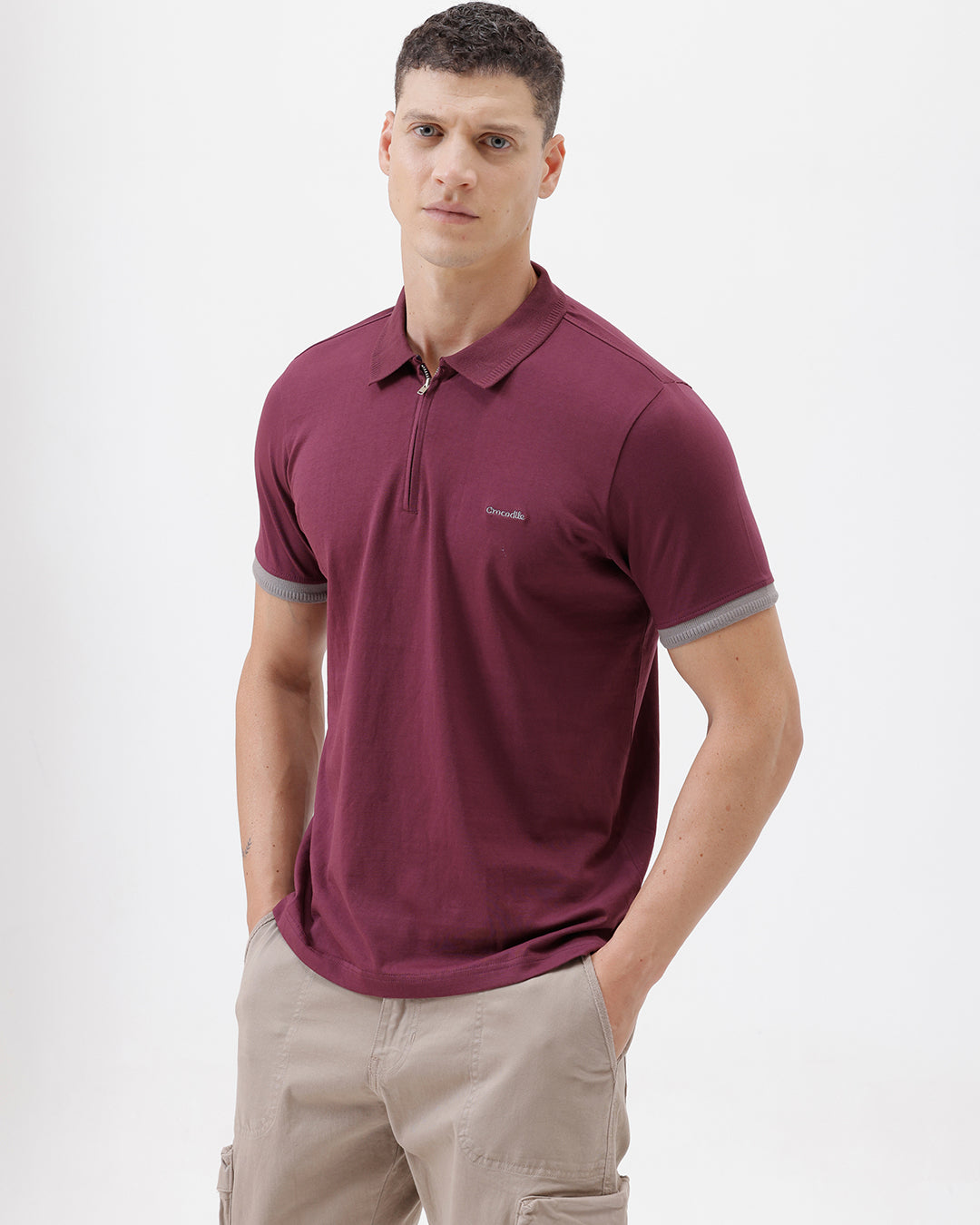 A man wearing a short-sleeve polo shirt in maroon with gray sleeve trim and a half-zip collar, paired with beige cargo pants, against a plain white studio background.