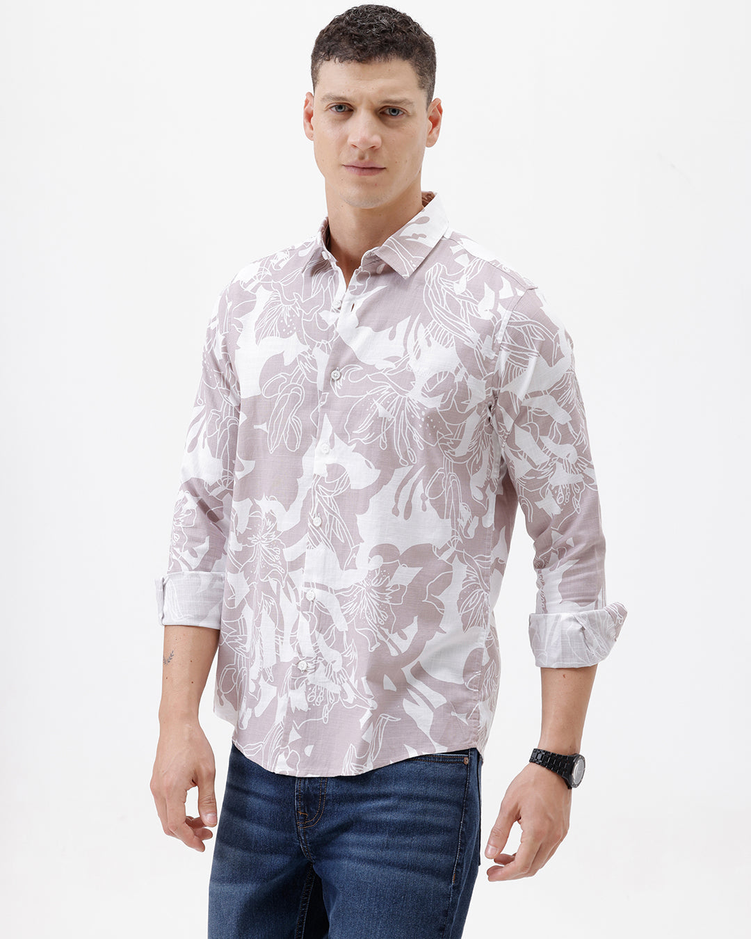 A man wearing a long-sleeve button-up shirt with a light gray and white abstract floral pattern, paired with dark blue jeans, standing against a plain white background.