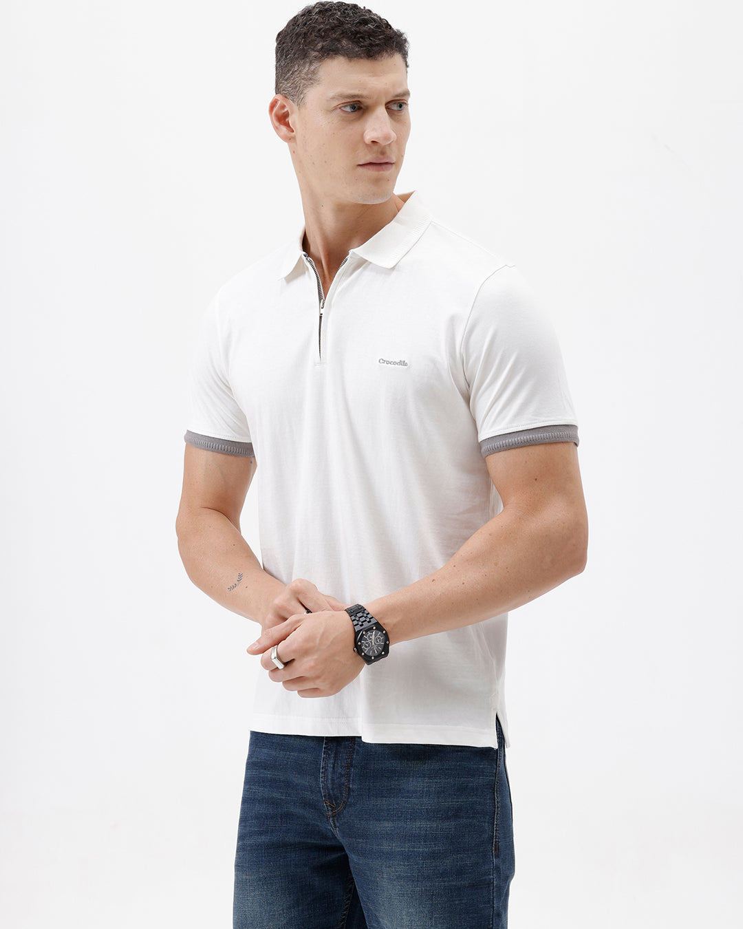 A man wearing a white short-sleeve polo shirt with gray ribbed trim on the collar and sleeve cuffs, paired with dark blue jeans, photographed against a plain white studio background.