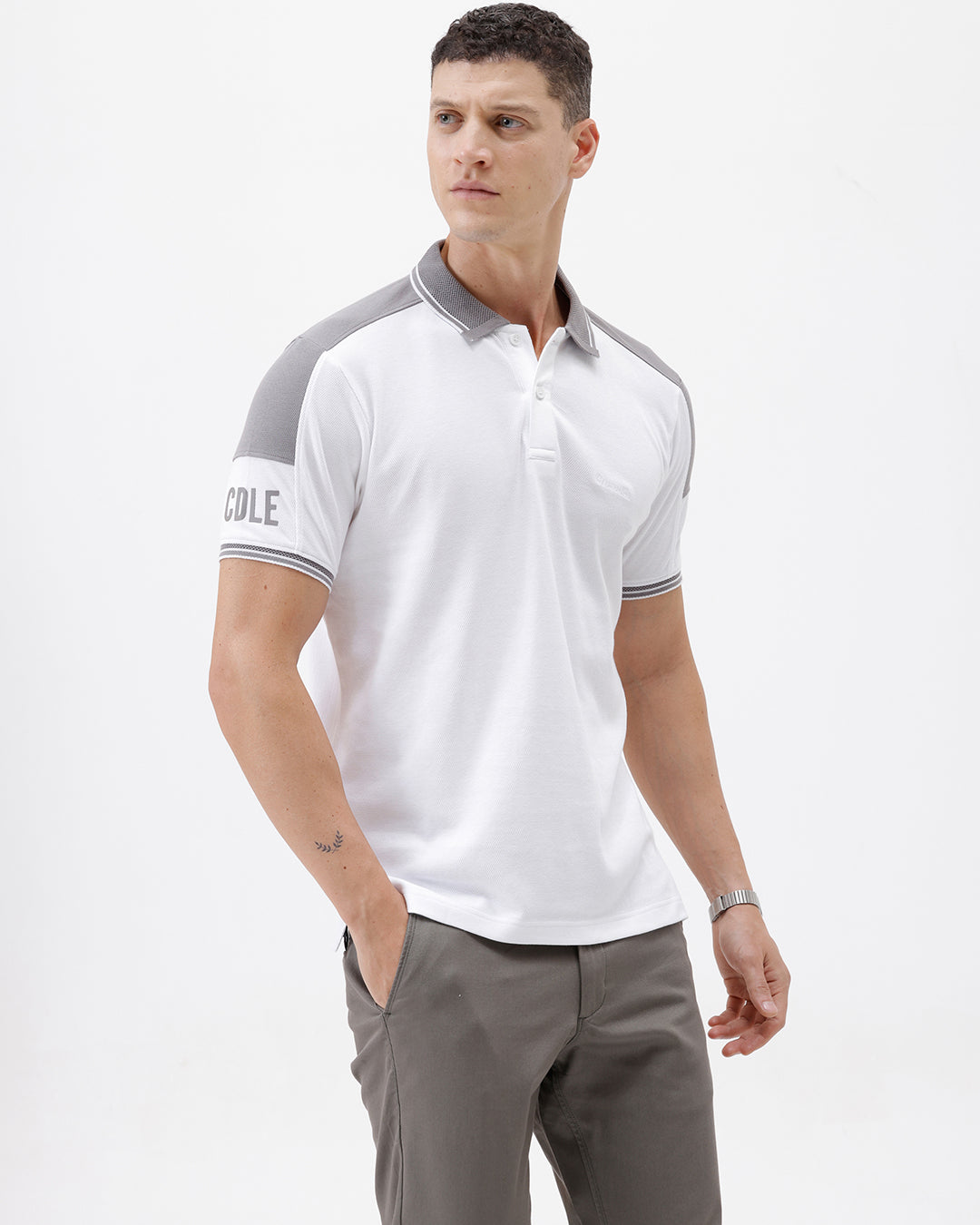 A man modeling a white short-sleeve polo shirt with gray shoulder panels and gray striped trim on the sleeves, paired with gray trousers and black sunglasses, against a plain white background.