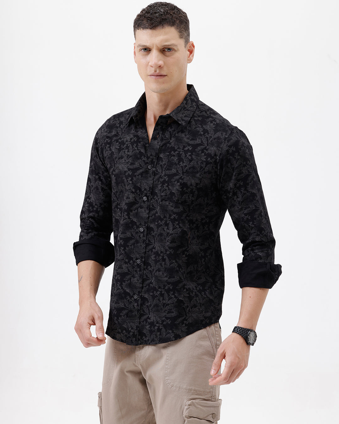 A man wearing a black long-sleeve button-up shirt with a subtle tonal floral pattern, paired with beige cargo pants and dark sunglasses, standing against a plain white background.