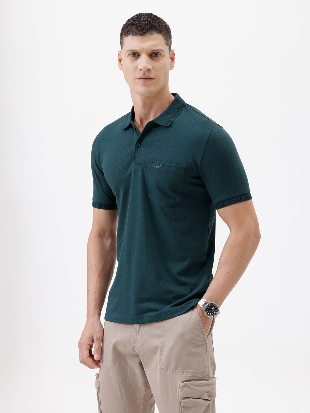 A man wearing a dark teal short-sleeve polo shirt with a chest pocket, paired with beige cargo pants, standing against a plain white studio background.