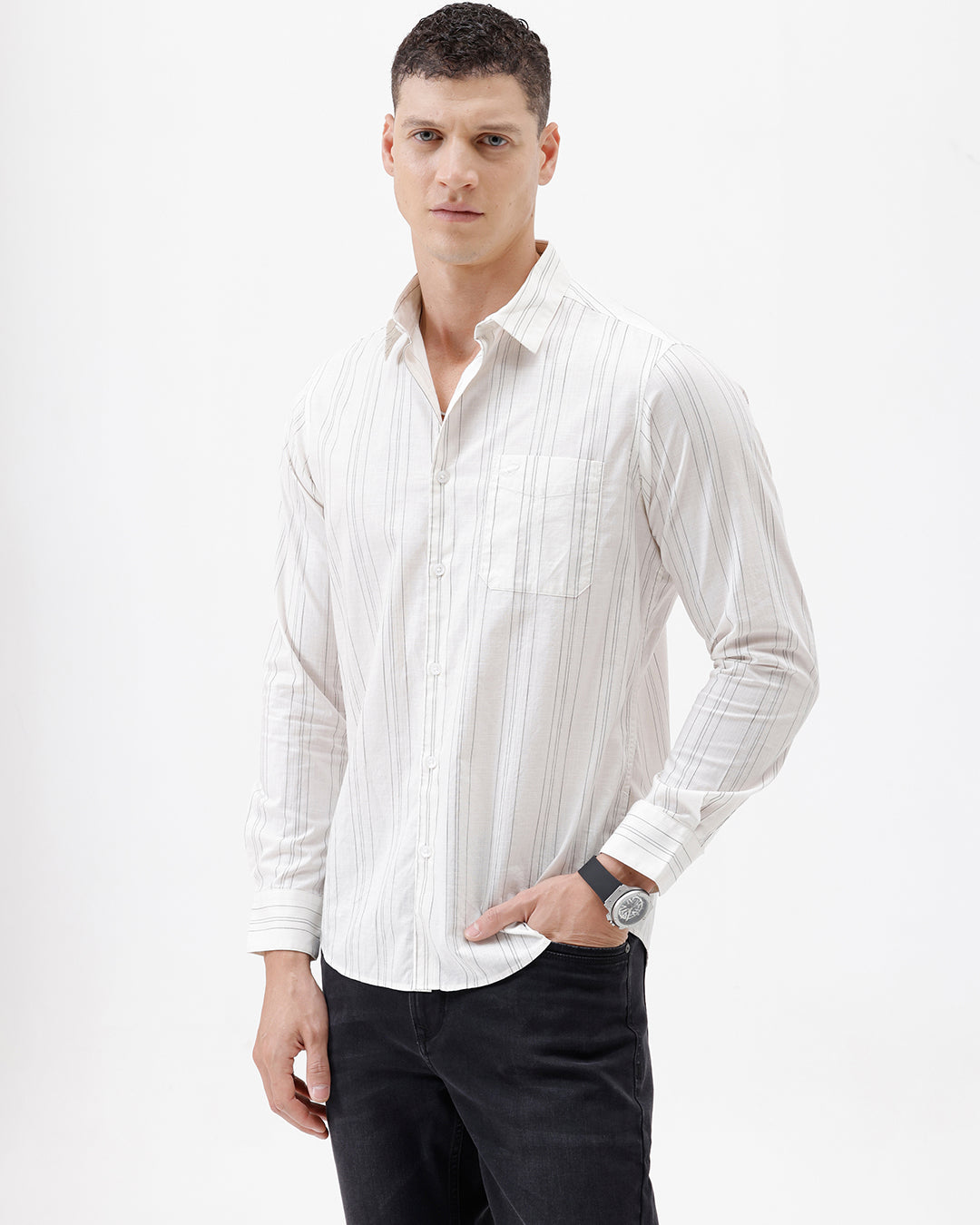 A man wearing a white long-sleeve button-up shirt with thin vertical gray stripes and black pants, standing against a plain white studio background.