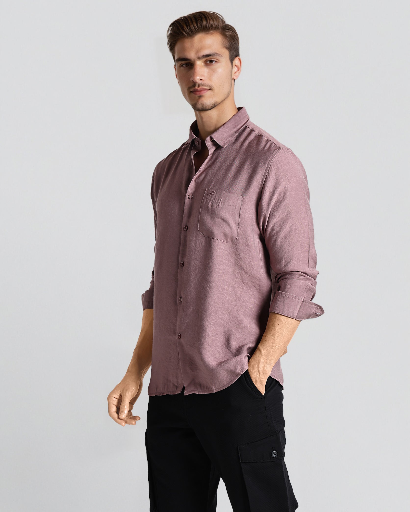 Man wearing a mauve button-up shirt and black pants on a light gray background