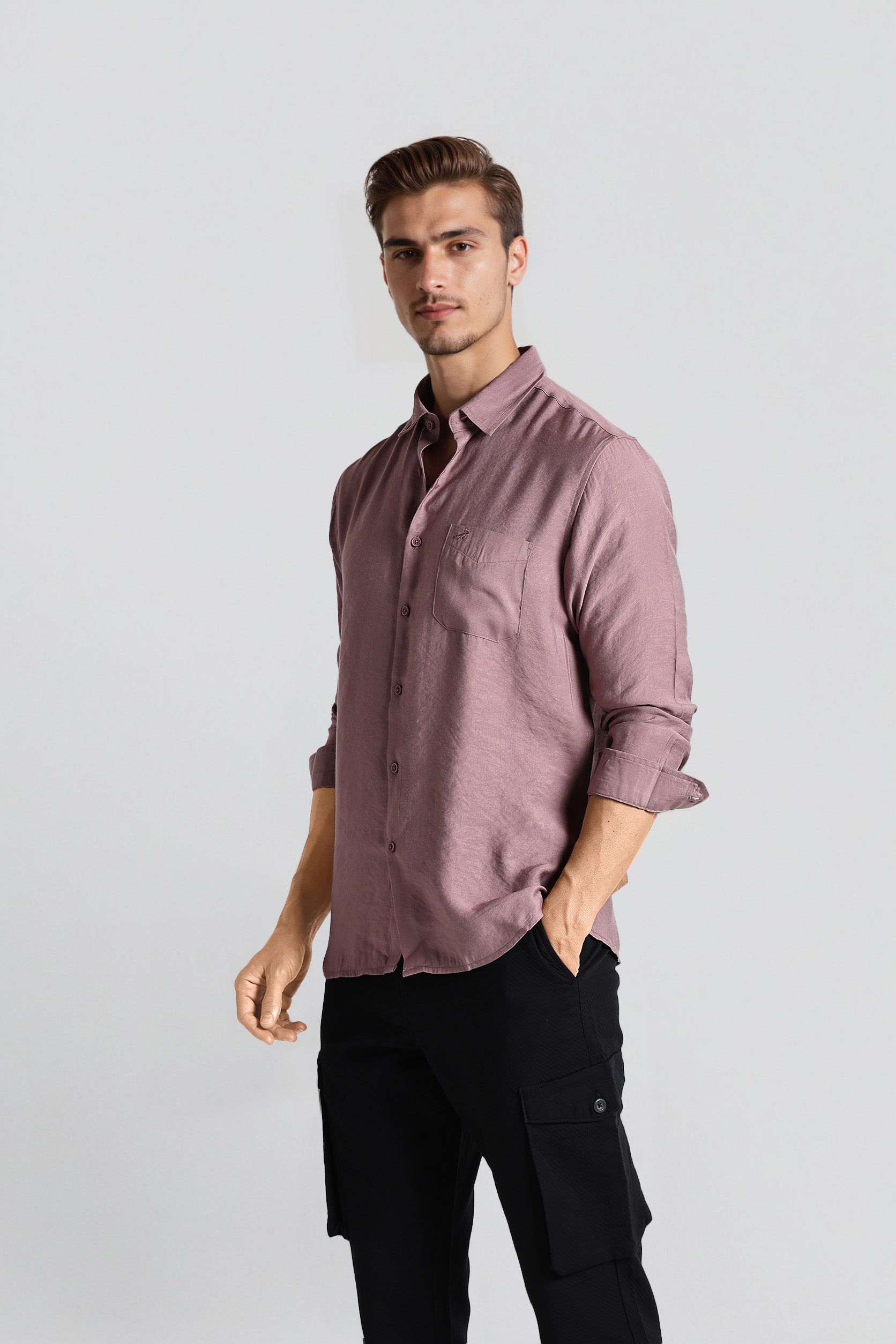 Man wearing a mauve button-up shirt and black pants on a light gray background