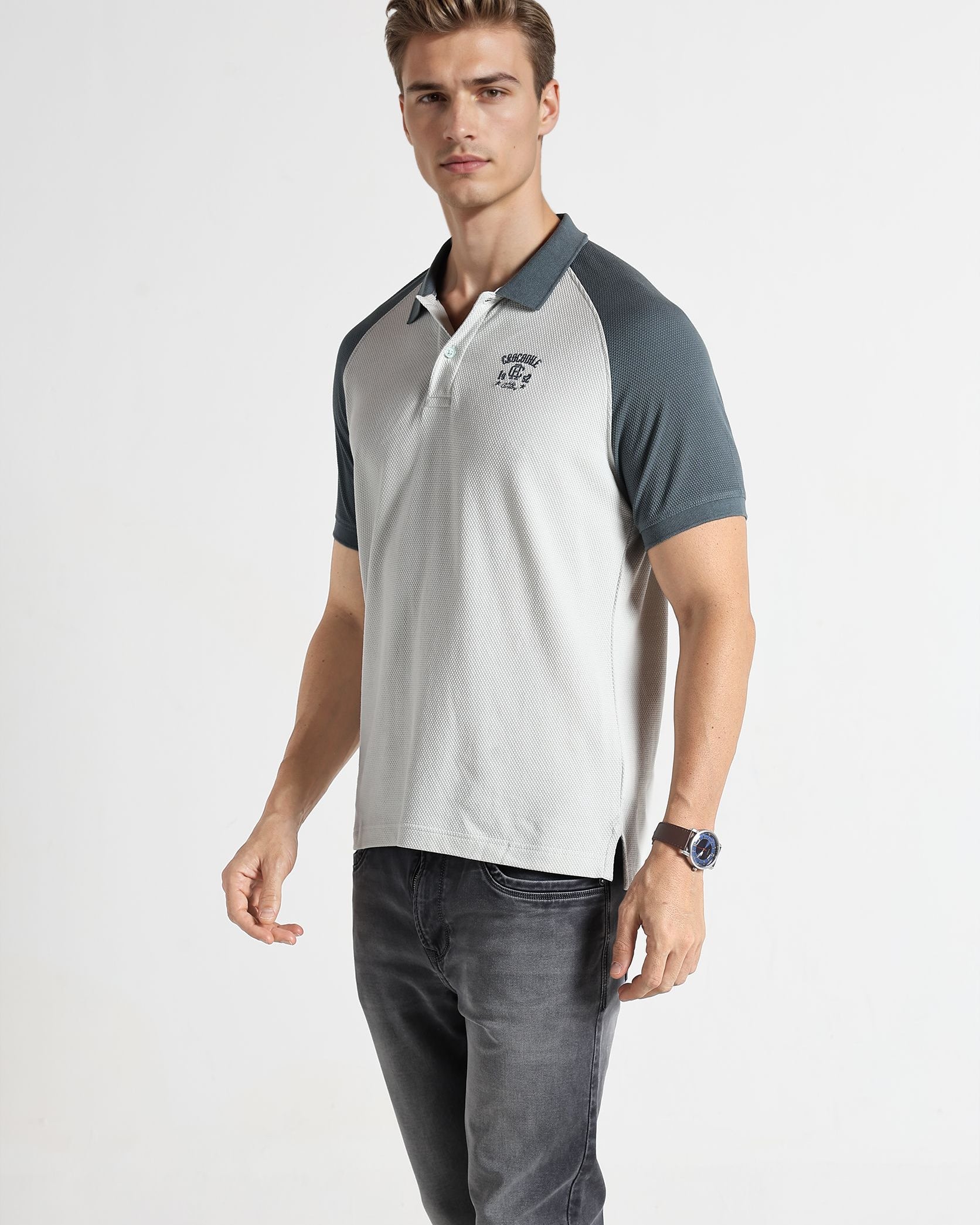 Man wearing a gray and white polo shirt with dark jeans on a white background