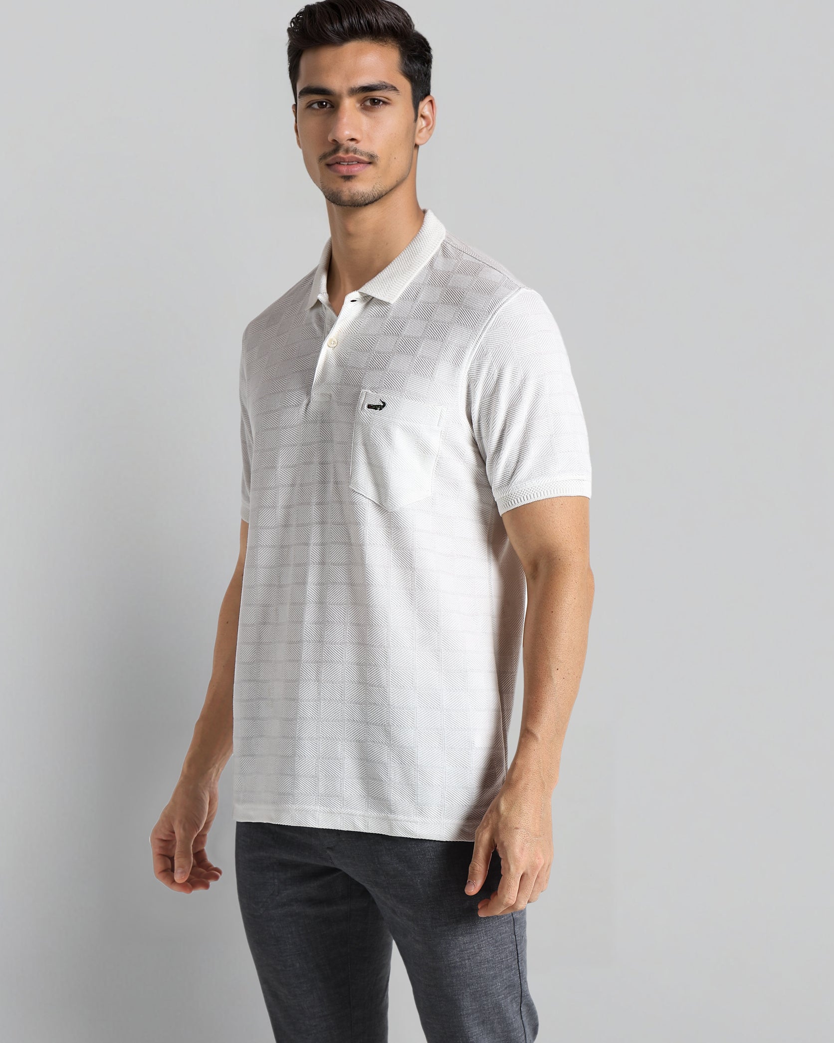 Man wearing a white polo shirt with a small logo on a gray background