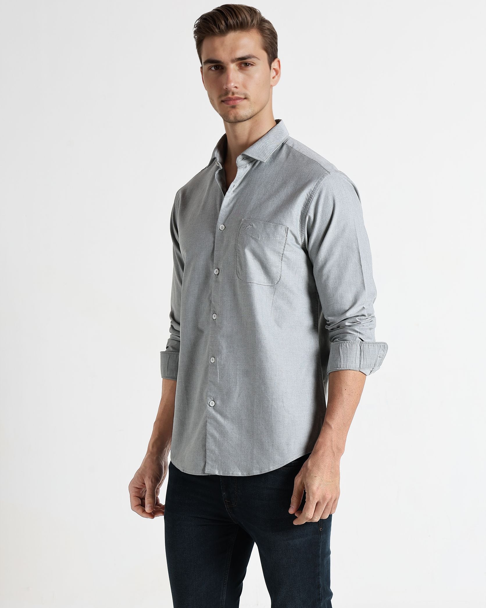 Man wearing a light gray button-up shirt and dark pants on a white background