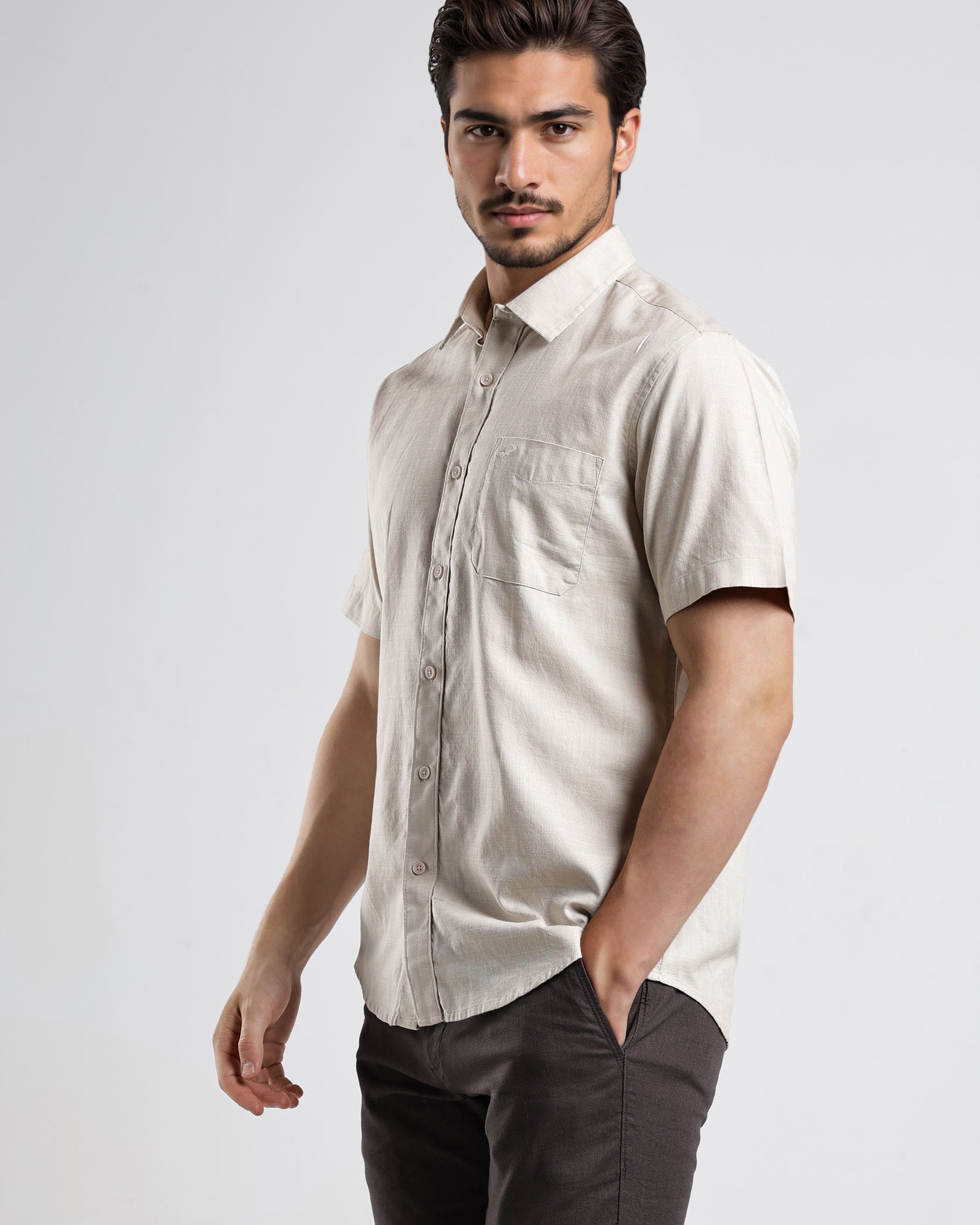 Man wearing a beige short-sleeve shirt and dark pants on a white background