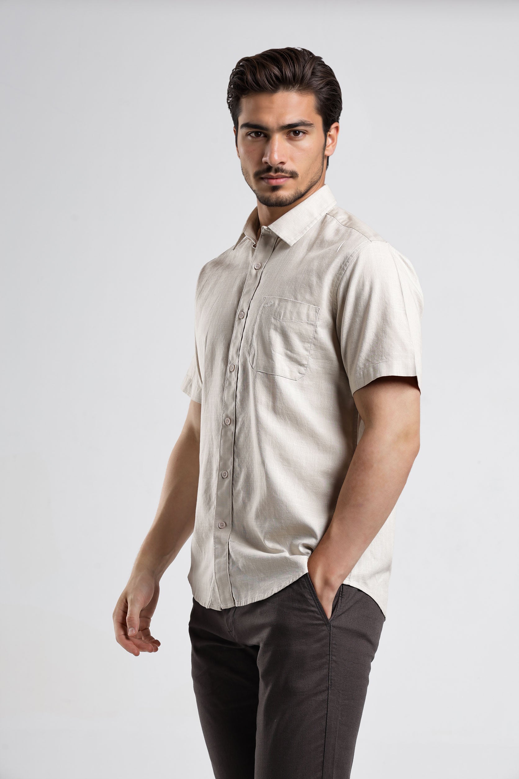 Man wearing a beige short-sleeve shirt and dark pants on a white background