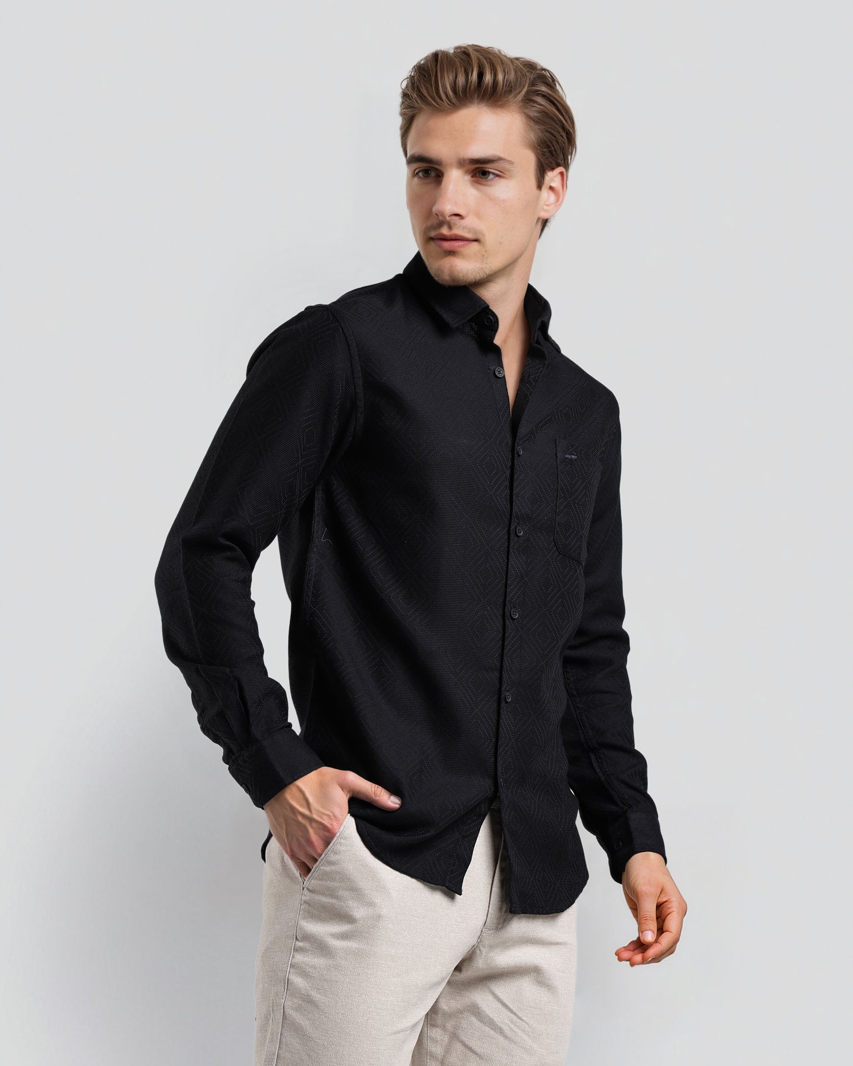 Man wearing a black shirt and light-colored pants against a white background