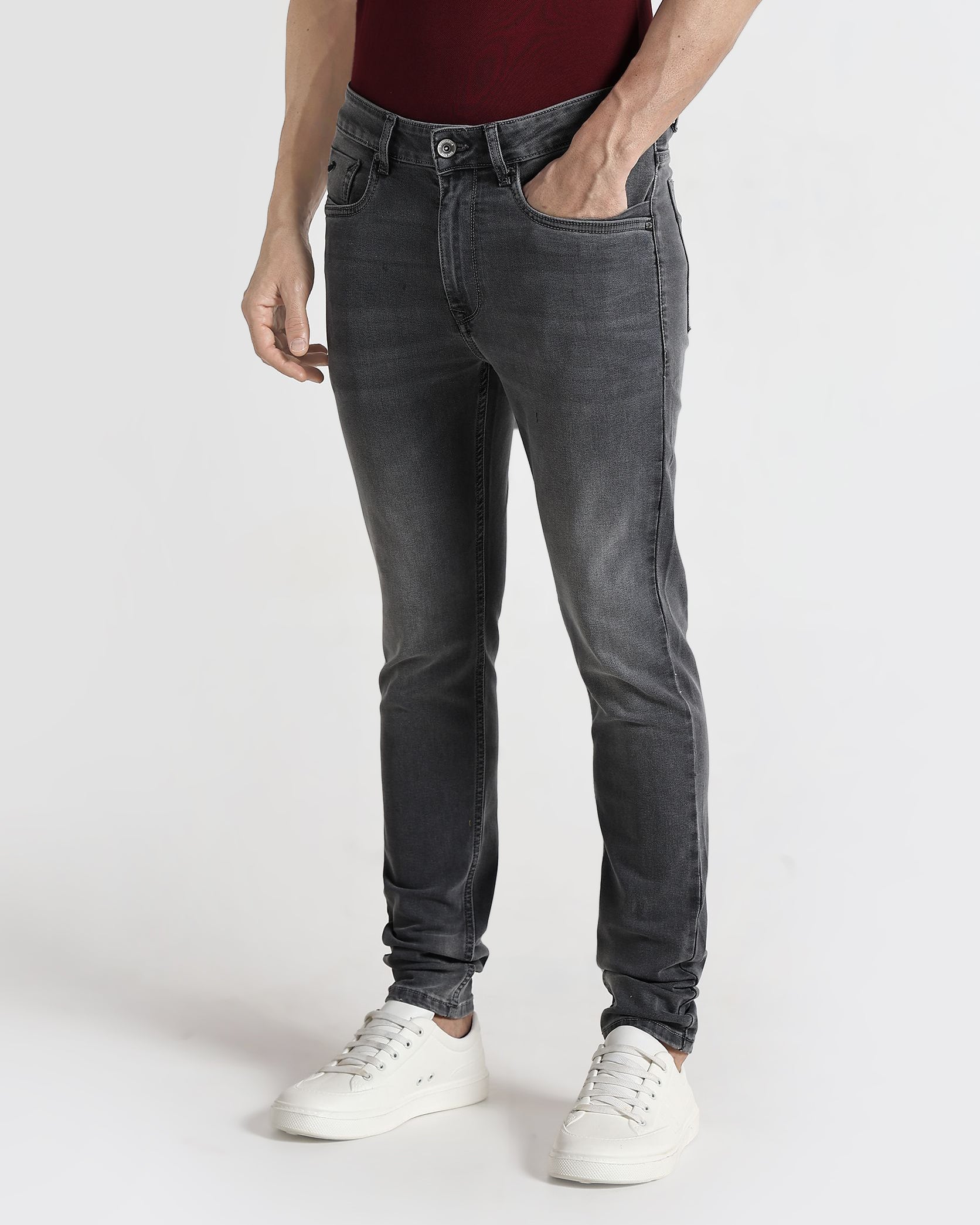 Person wearing dark gray jeans and white sneakers on a white background