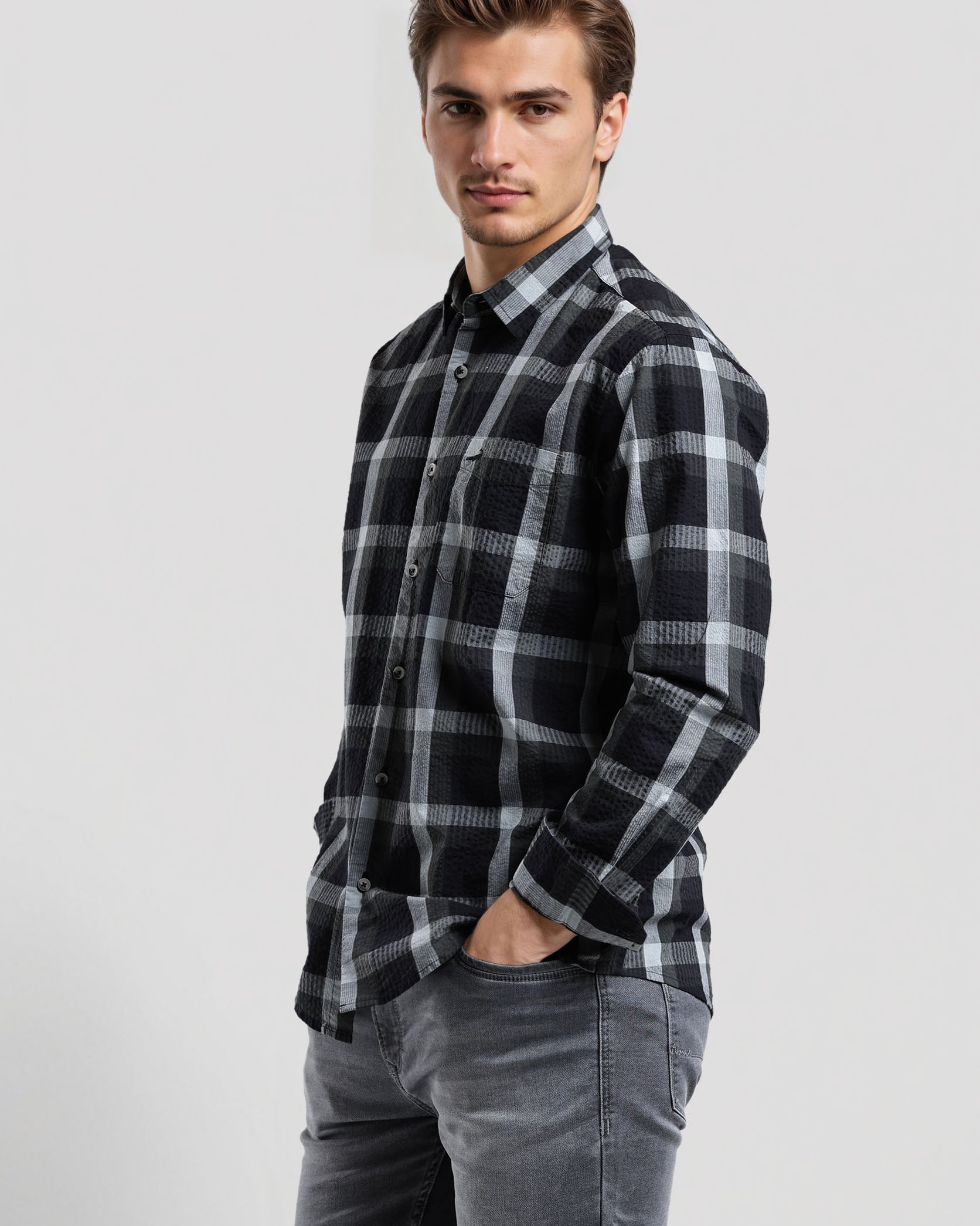Man wearing a black and gray plaid shirt with gray jeans on a white background