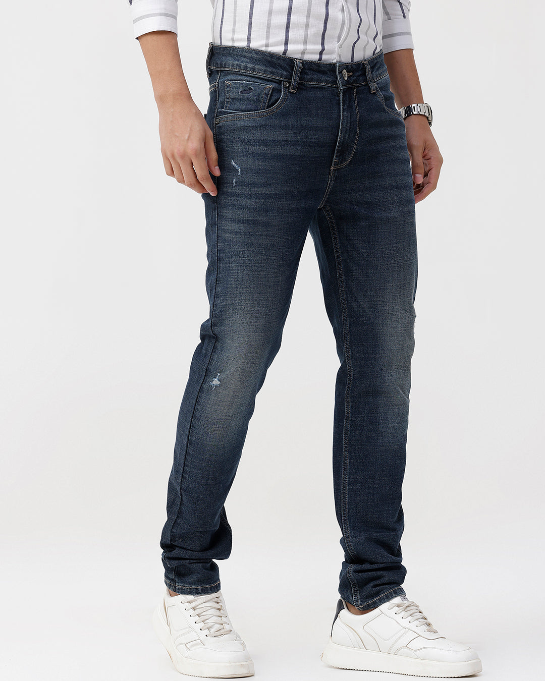 Person wearing dark blue jeans and white sneakers on a white background