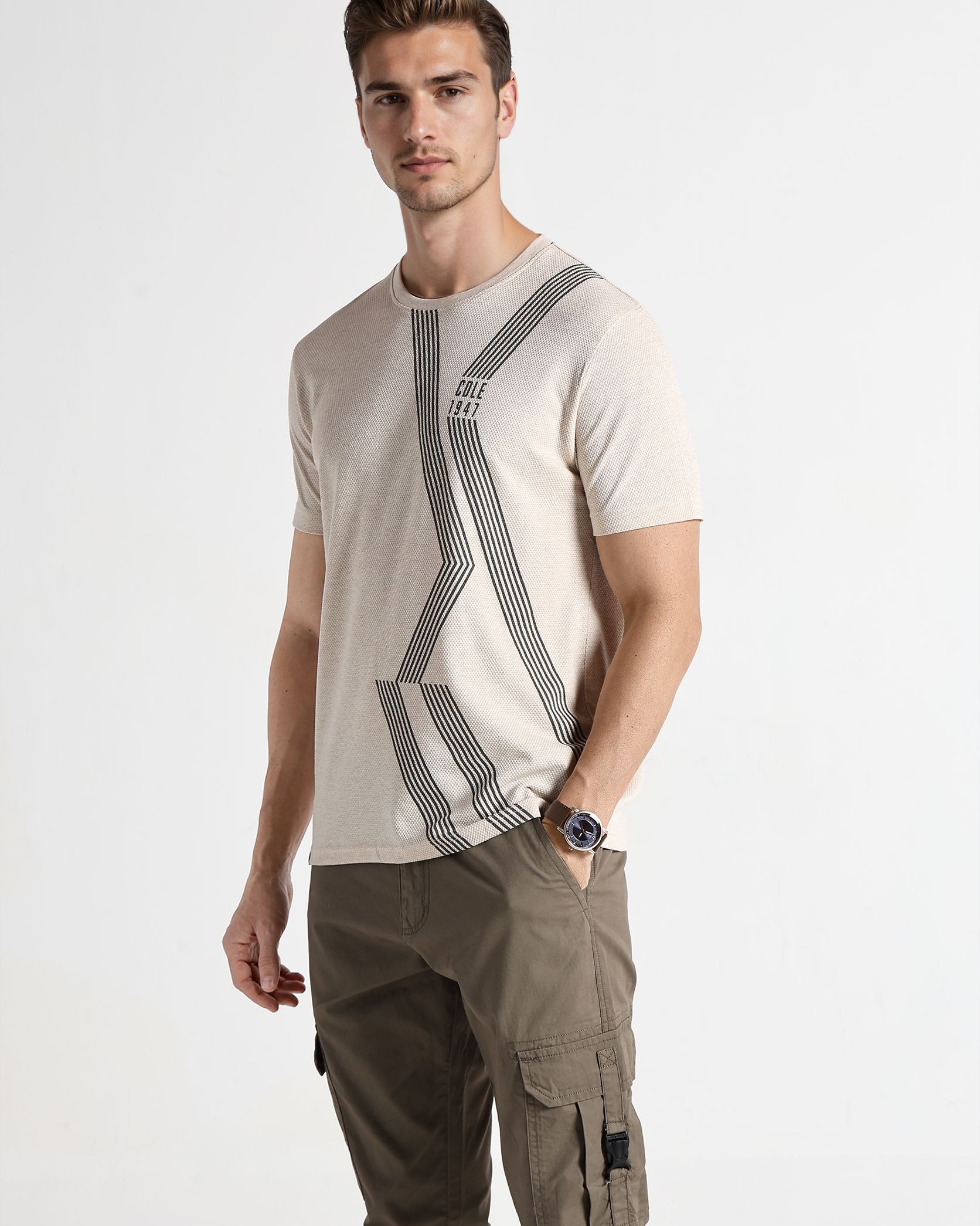 Man wearing a beige t-shirt with graphic design and cargo pants on a white background