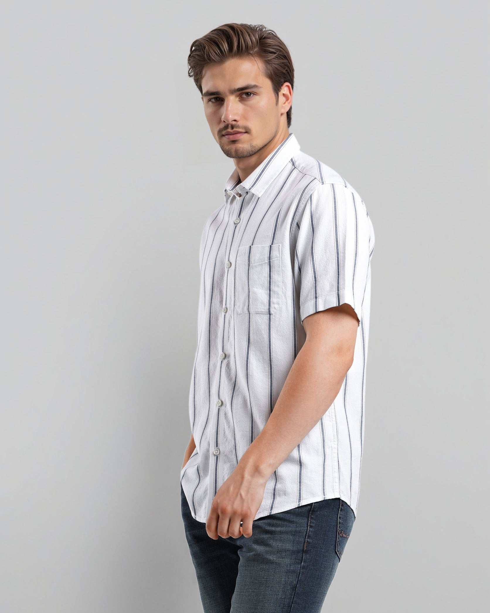 Man wearing a white striped shirt and dark jeans against a gray background