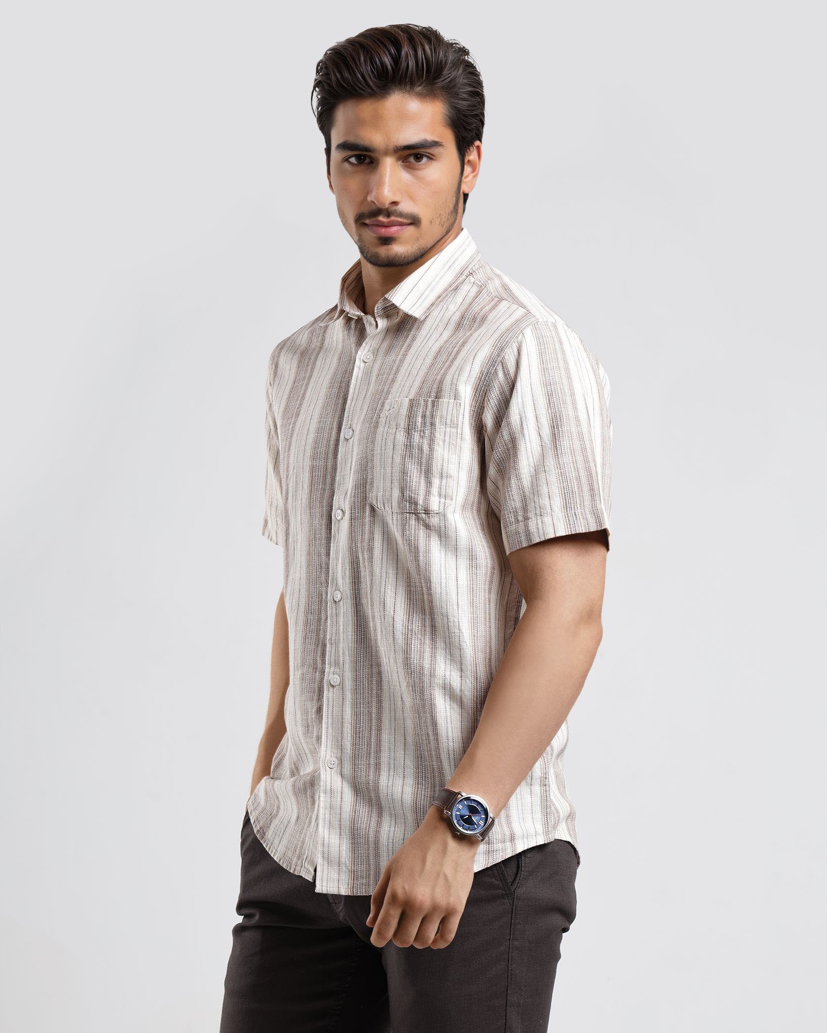 Man wearing a striped shirt and dark pants on a light gray background