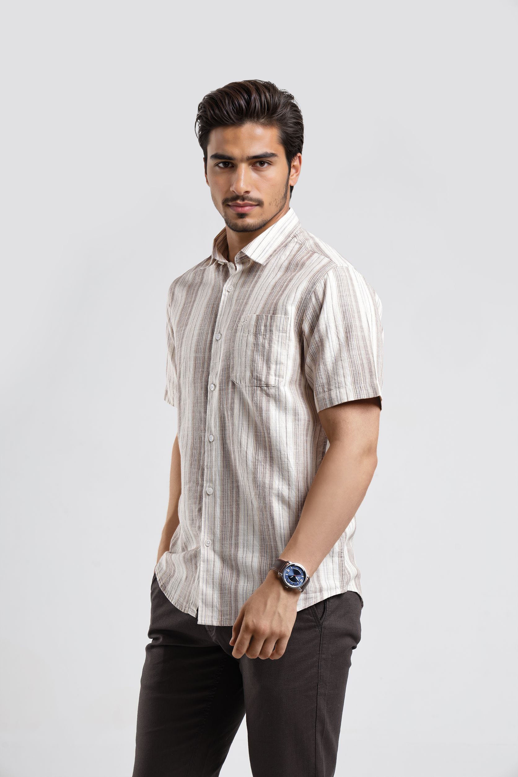 Man wearing a striped shirt and dark pants on a light gray background