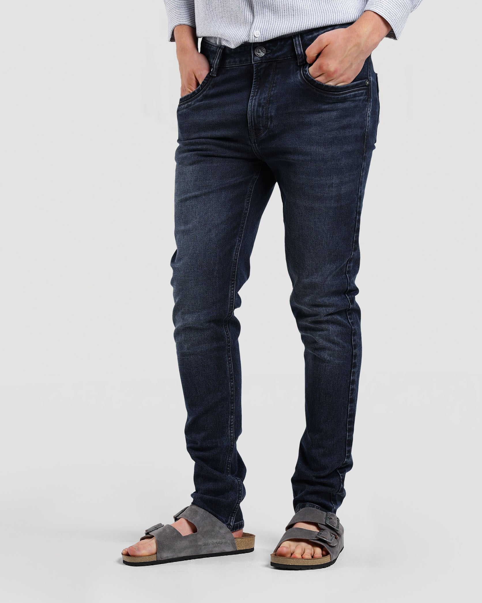 Person wearing dark blue jeans and sandals on a plain background