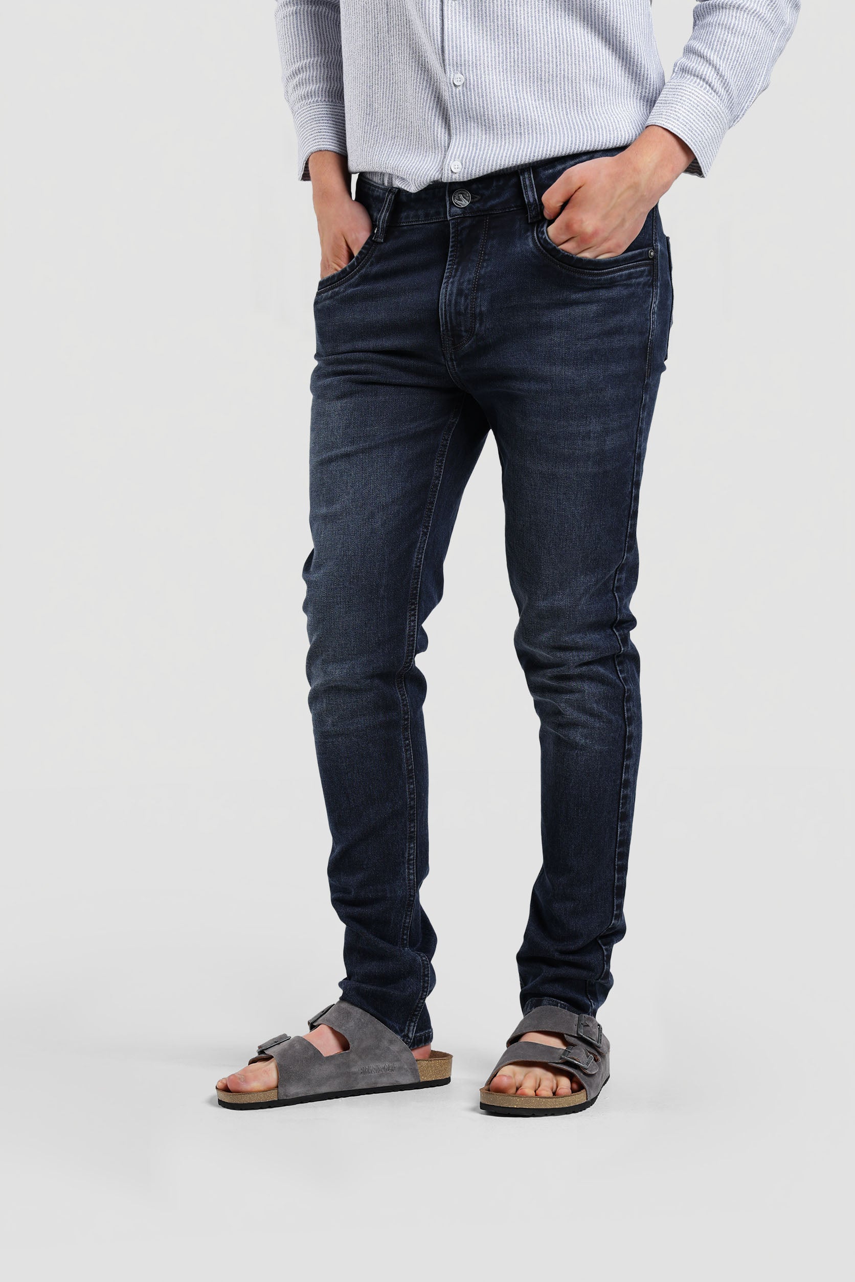 Person wearing dark blue jeans and sandals on a plain background