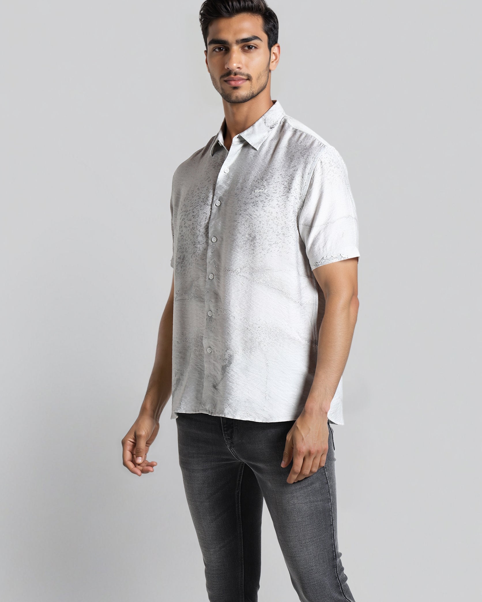 Man wearing a white short-sleeve shirt and dark jeans on a gray background