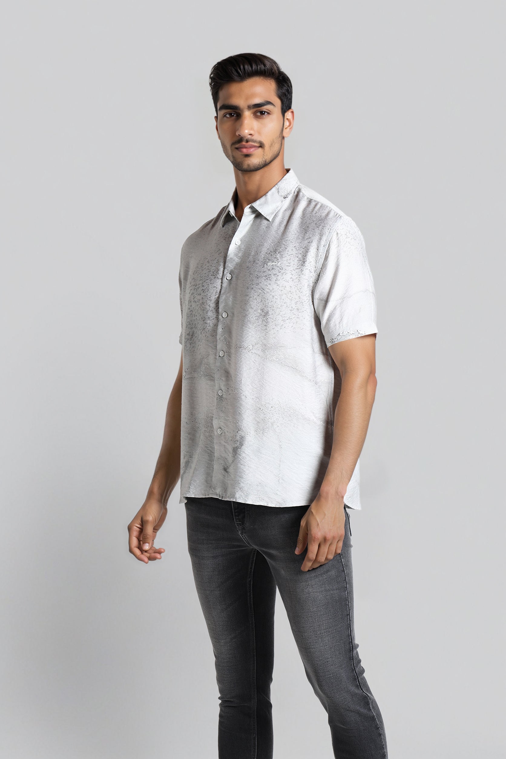 Man wearing a white short-sleeve shirt and dark jeans on a gray background