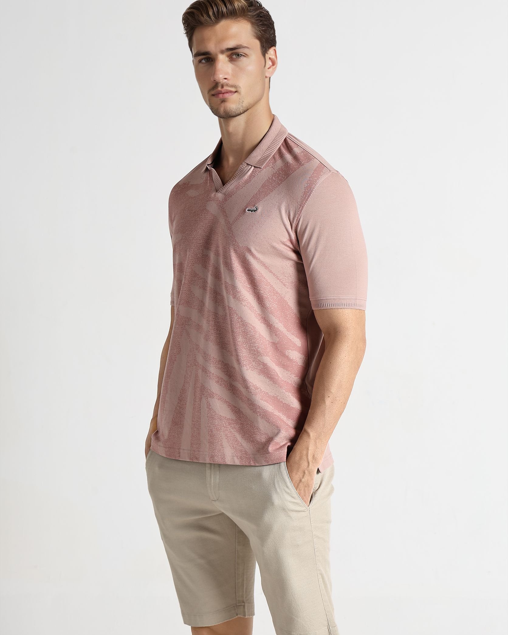 Man wearing a pink polo shirt and beige shorts on a white background