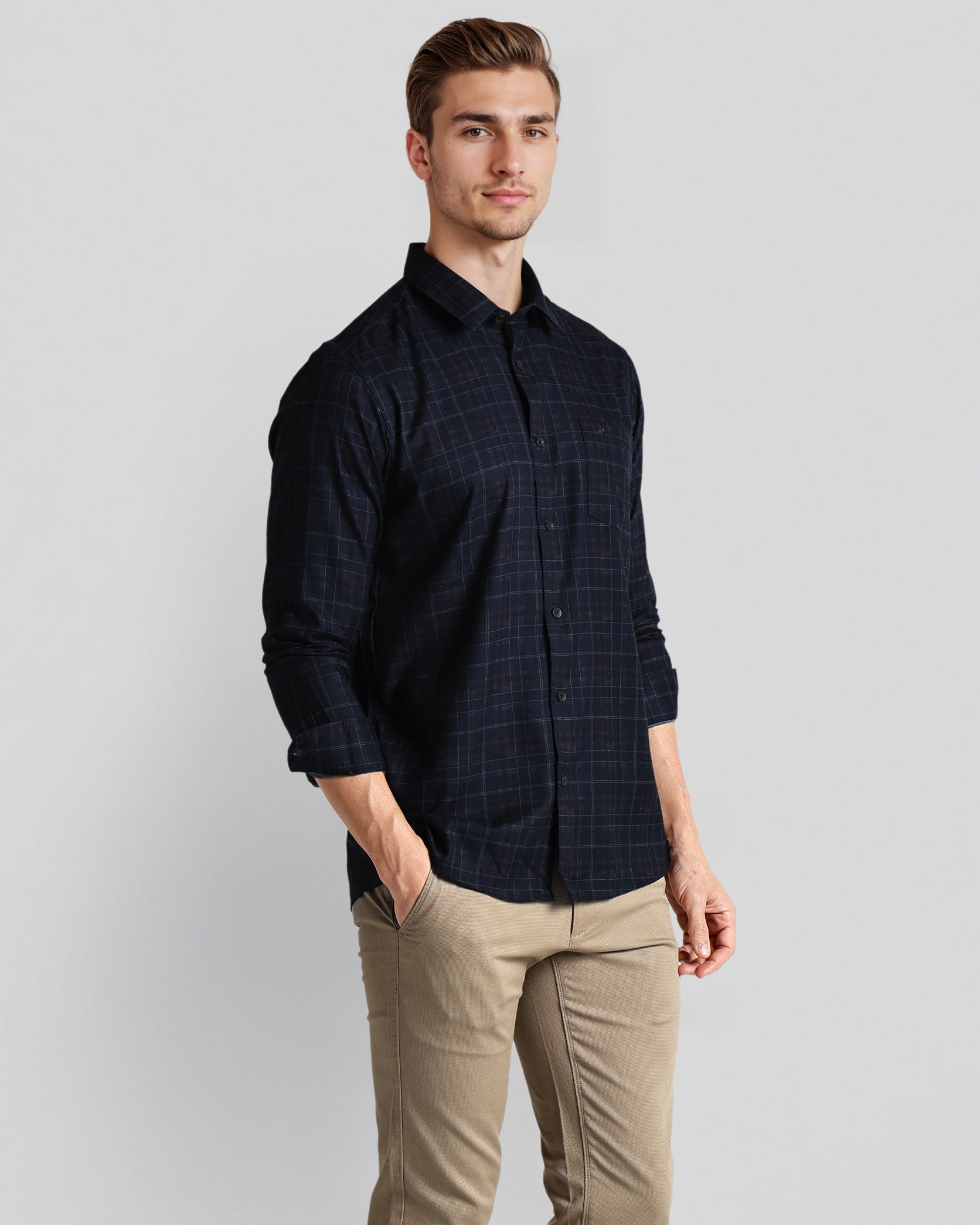 Man wearing a dark plaid shirt and beige pants on a light gray background