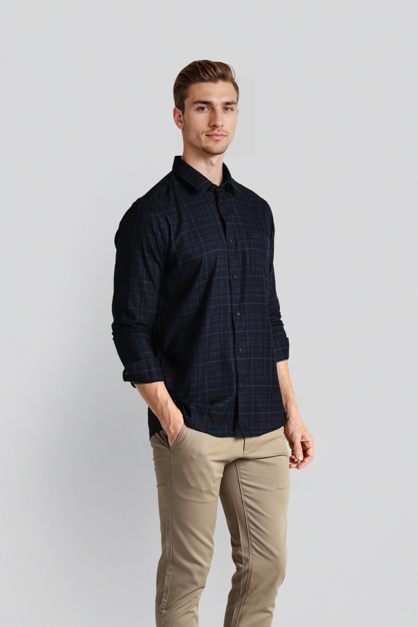 Man wearing a dark plaid shirt and beige pants on a light gray background