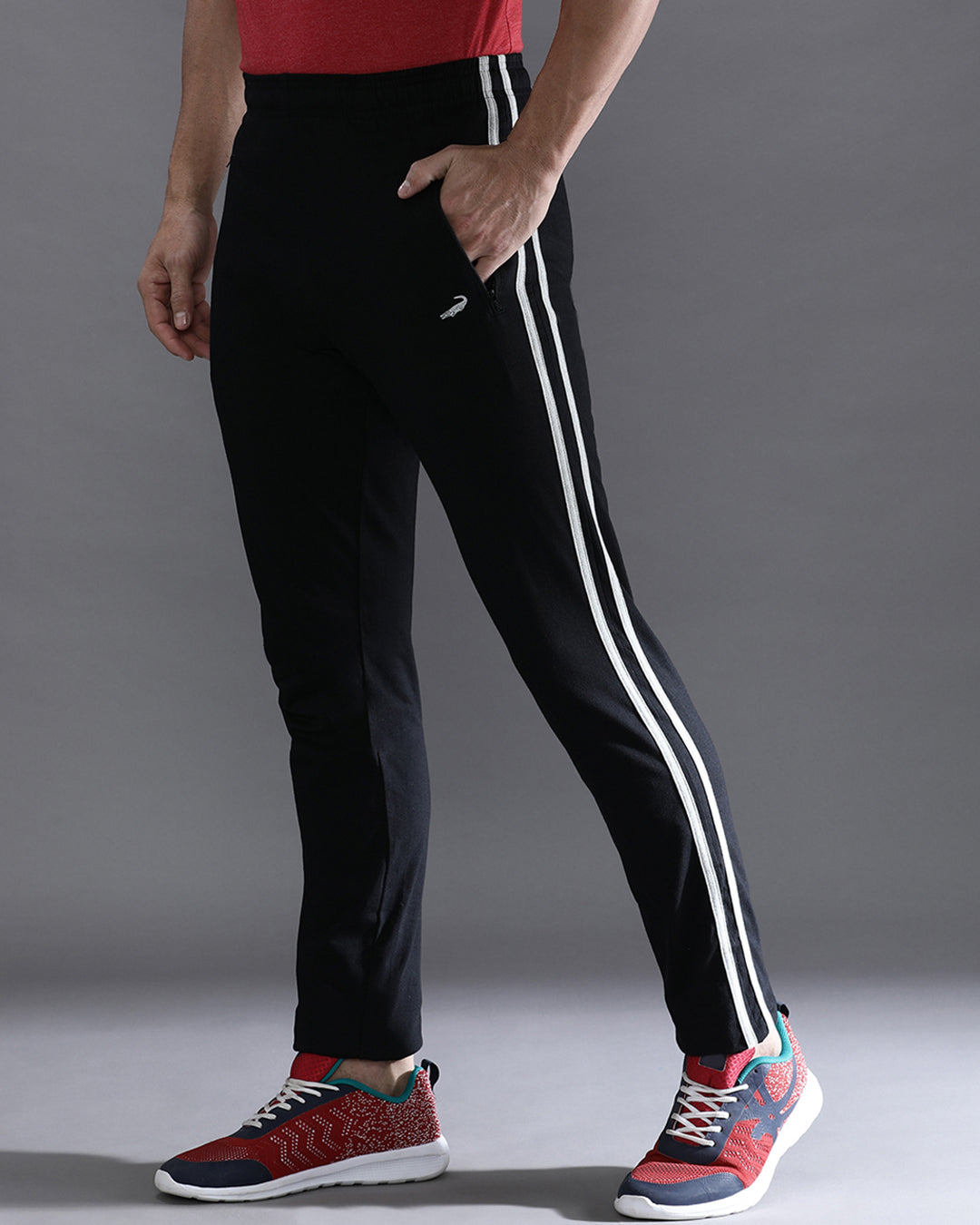 Person wearing black pants with white stripes and colorful sneakers on a gray background