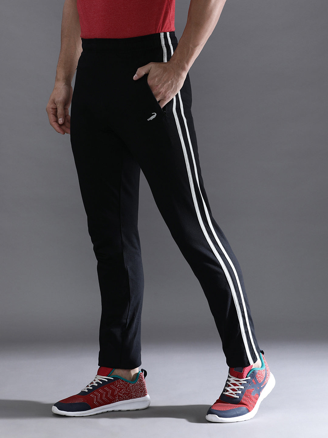 Person wearing black pants with white stripes and colorful sneakers on a gray background