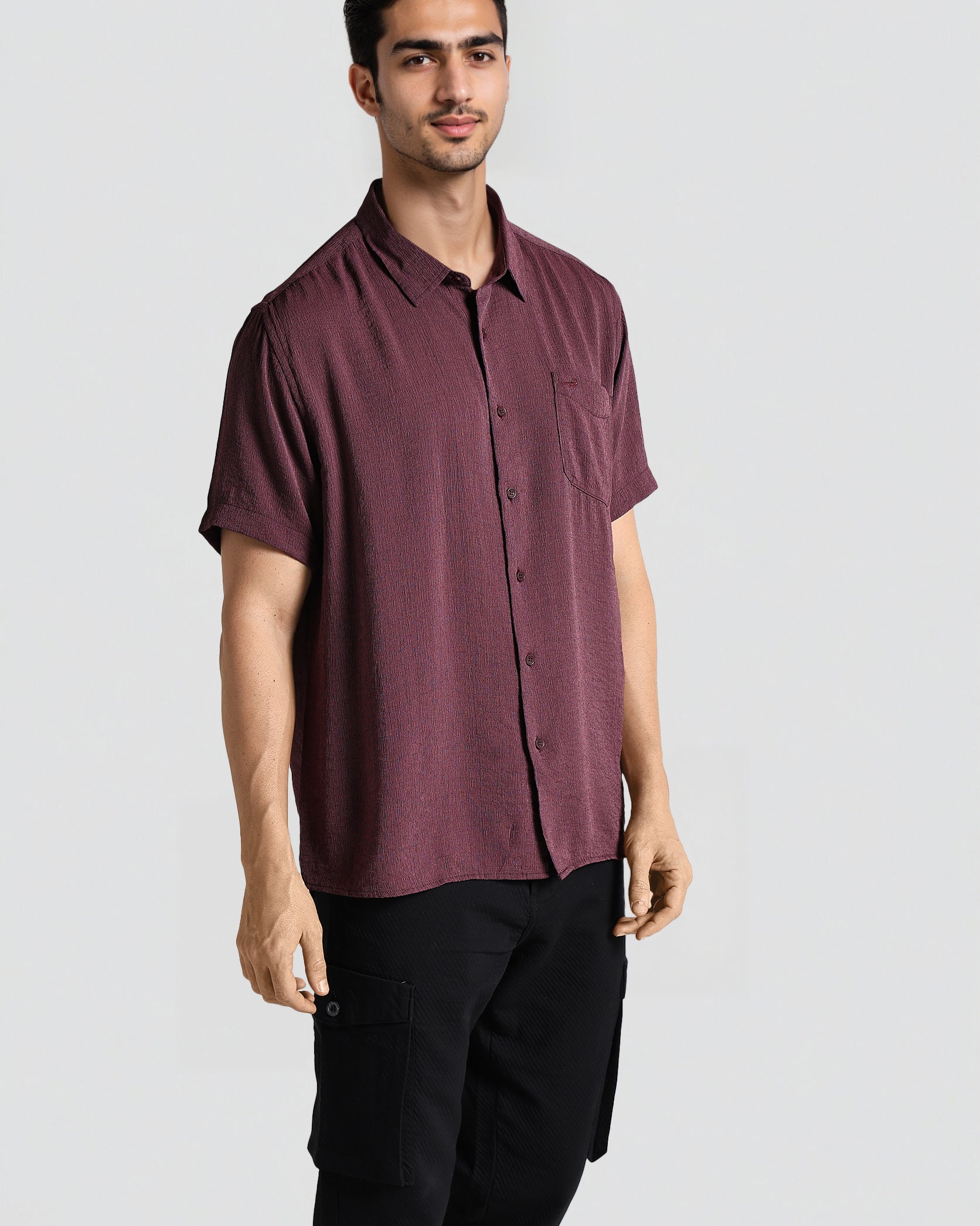 Man wearing a maroon button-up shirt and black pants on a white background