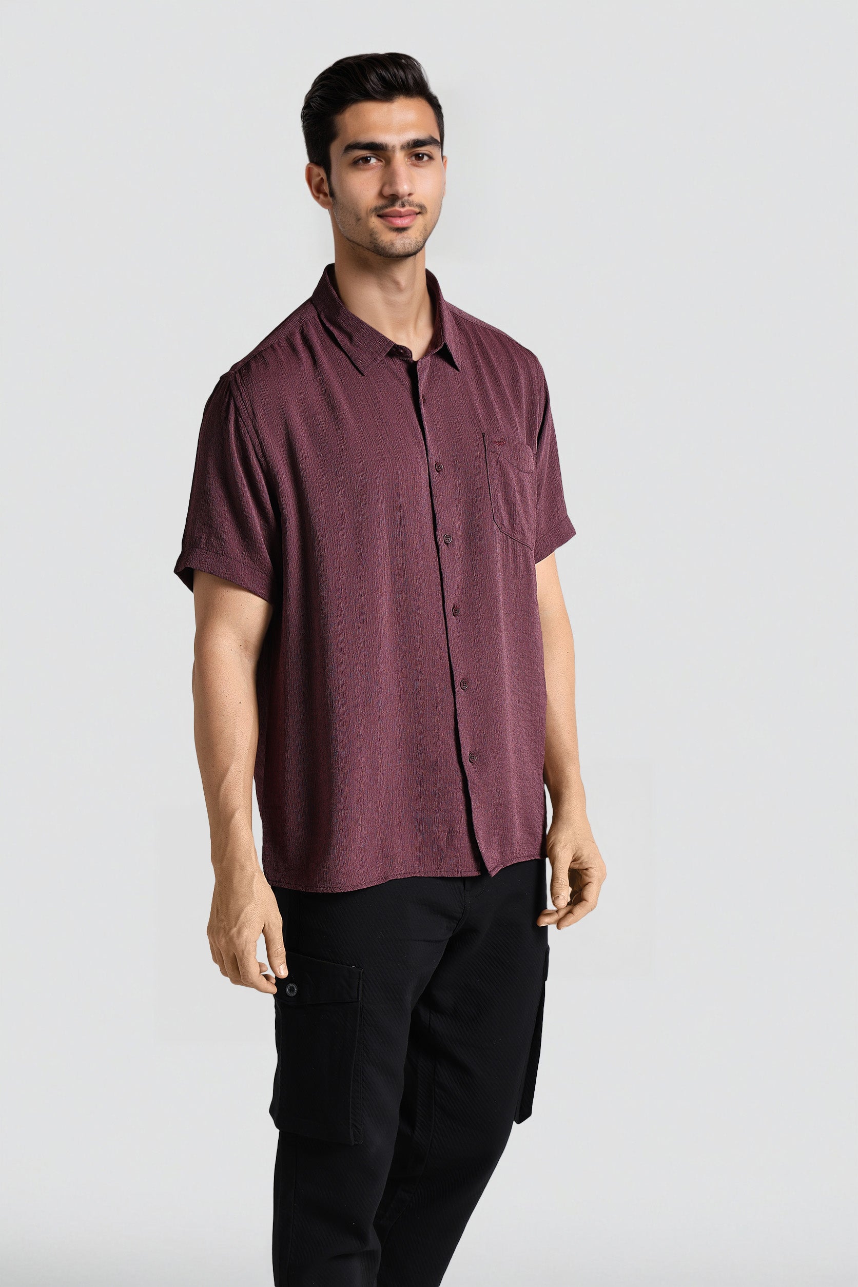 Man wearing a maroon button-up shirt and black pants on a white background