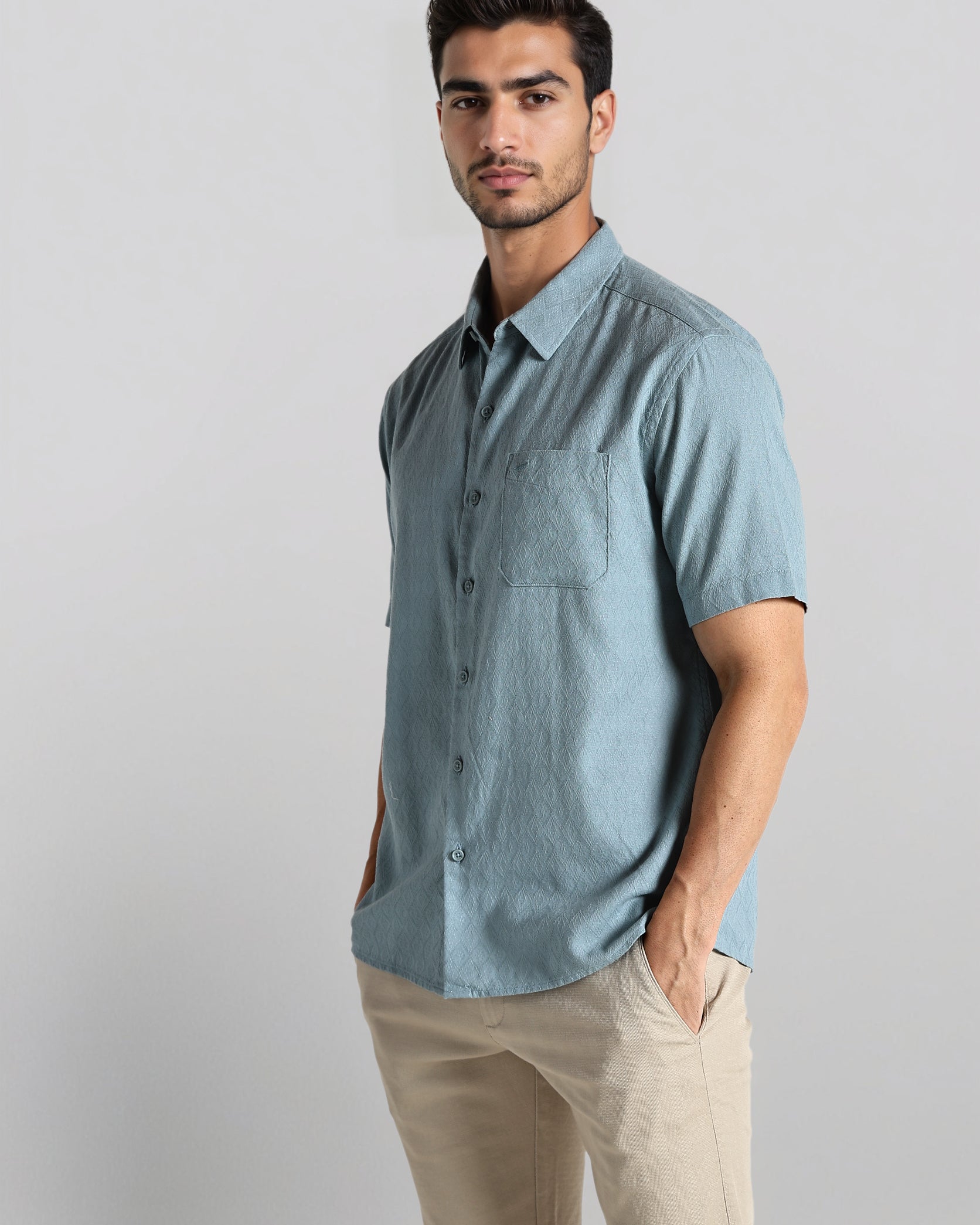 Man wearing a light blue button-up shirt and beige shorts on a gray background