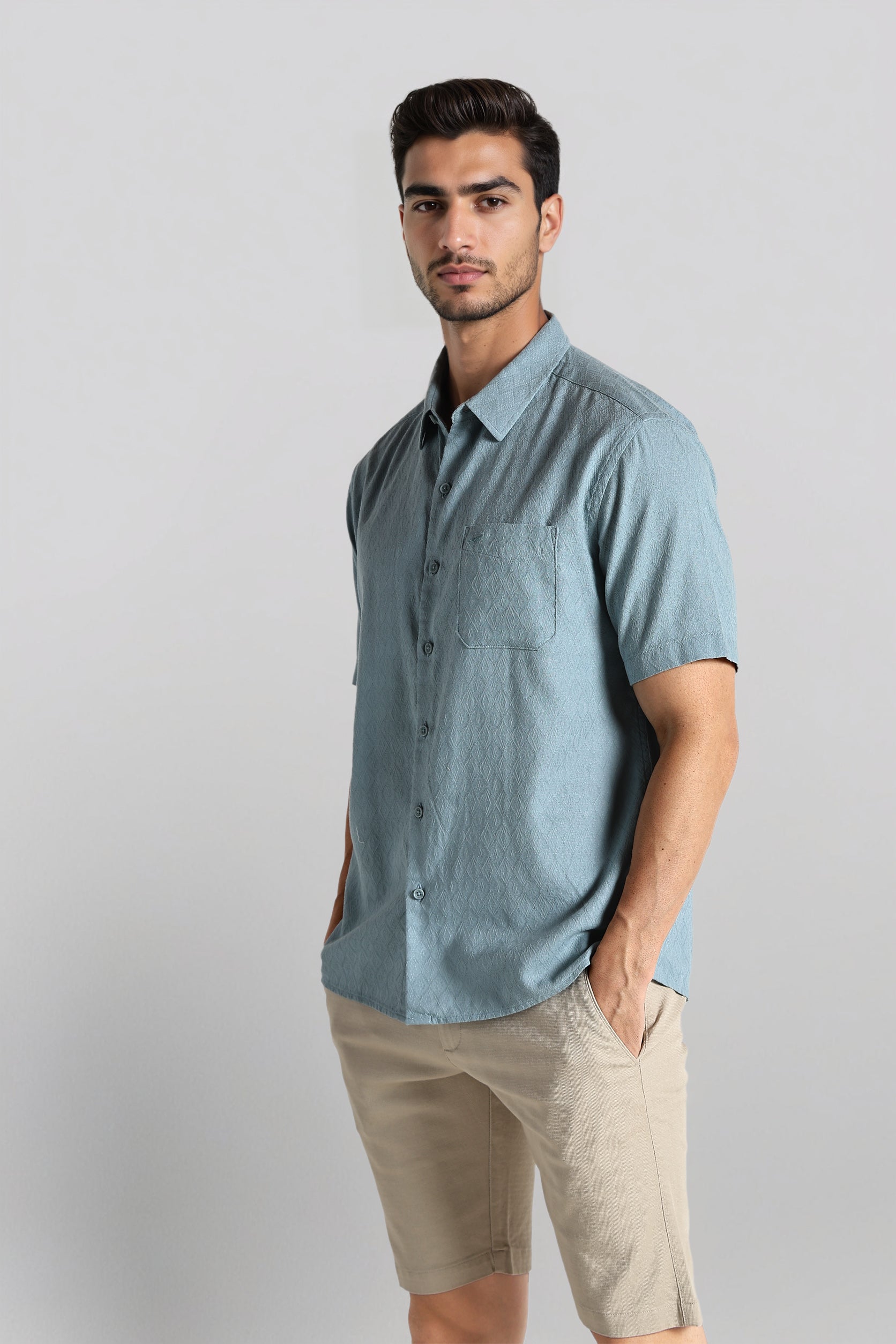 Man wearing a light blue button-up shirt and beige shorts on a gray background