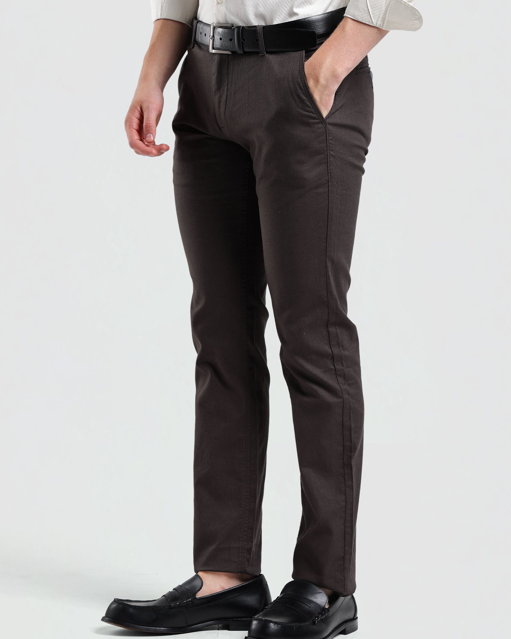 Person wearing brown dress pants with a white shirt and black loafers on a light gray background