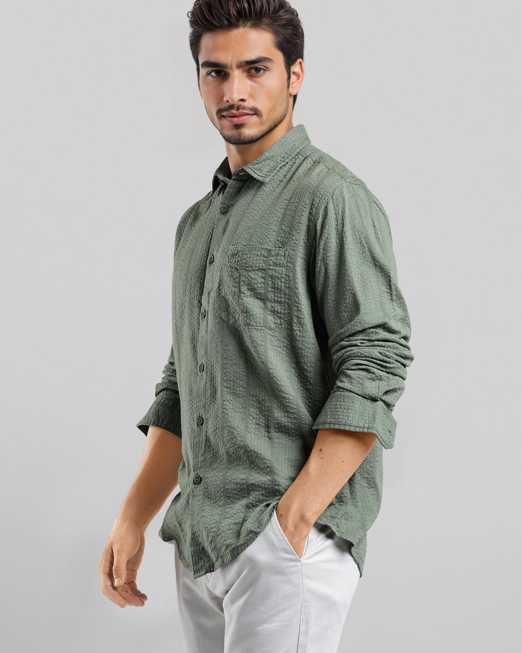 Man wearing a green checkered shirt and white pants on a gray background