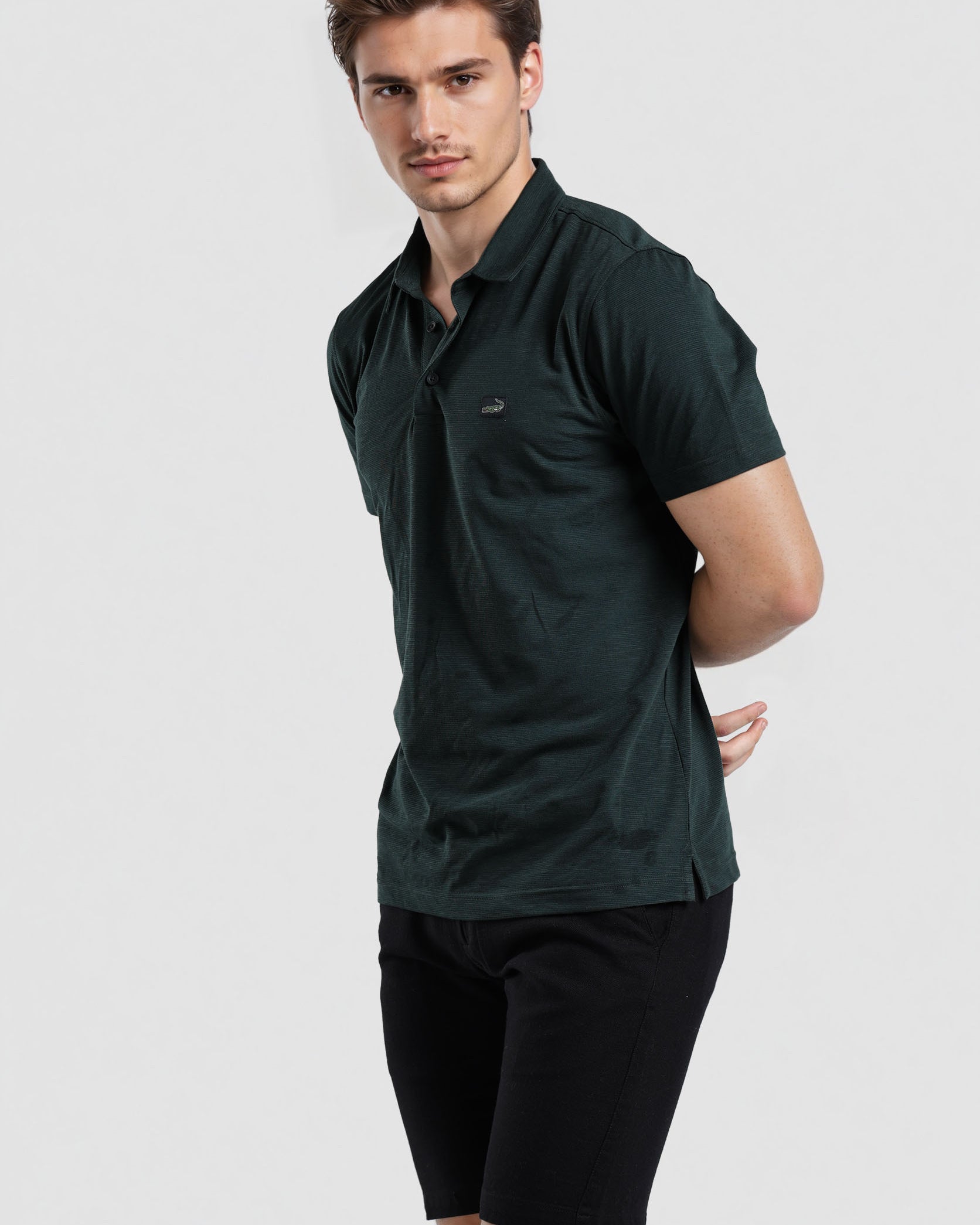 Man wearing a dark green polo shirt and black shorts on a light gray background
