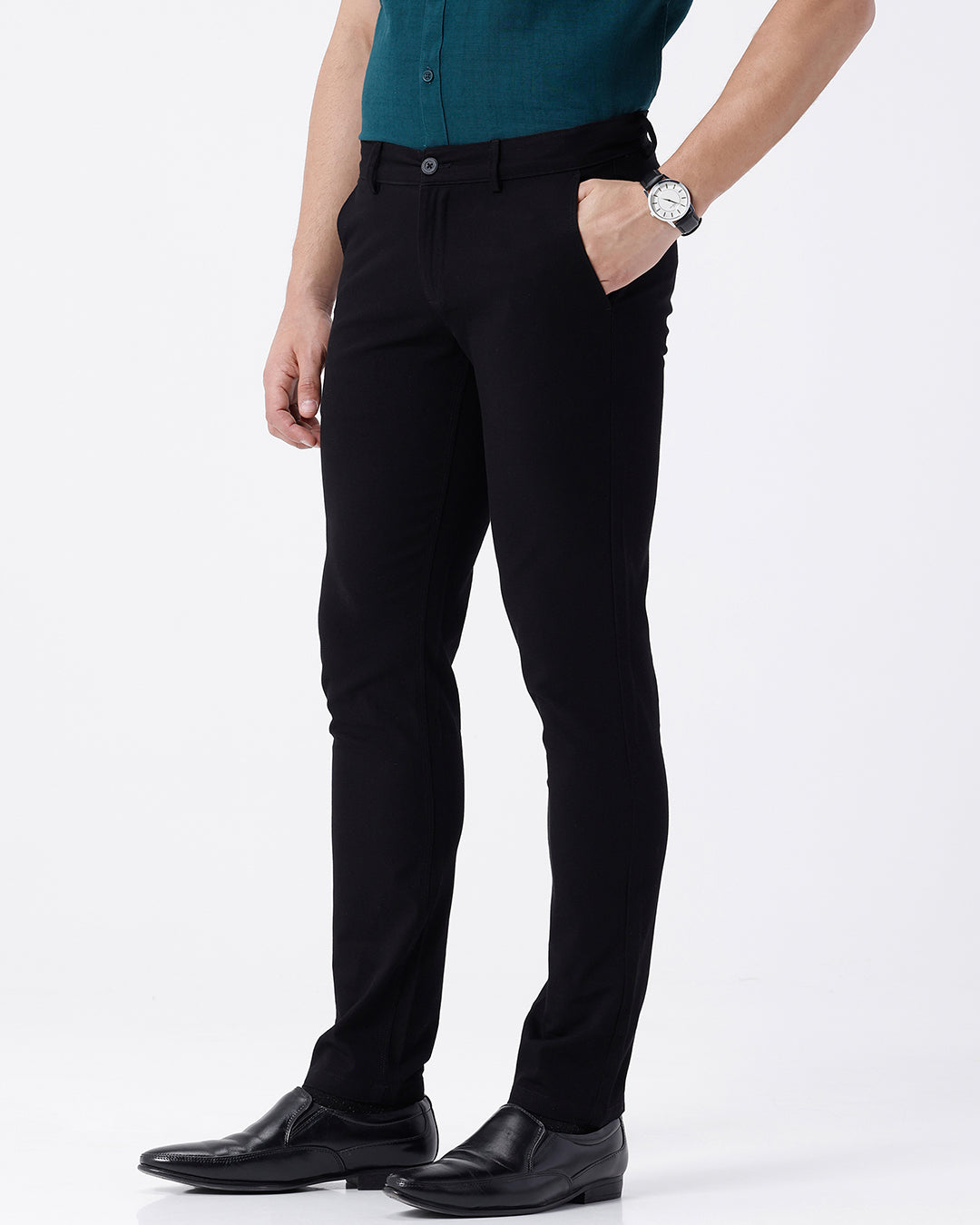 A man wearing slim-fit black trousers, a teal button-down shirt, and black leather dress shoes, standing against a plain white studio background.