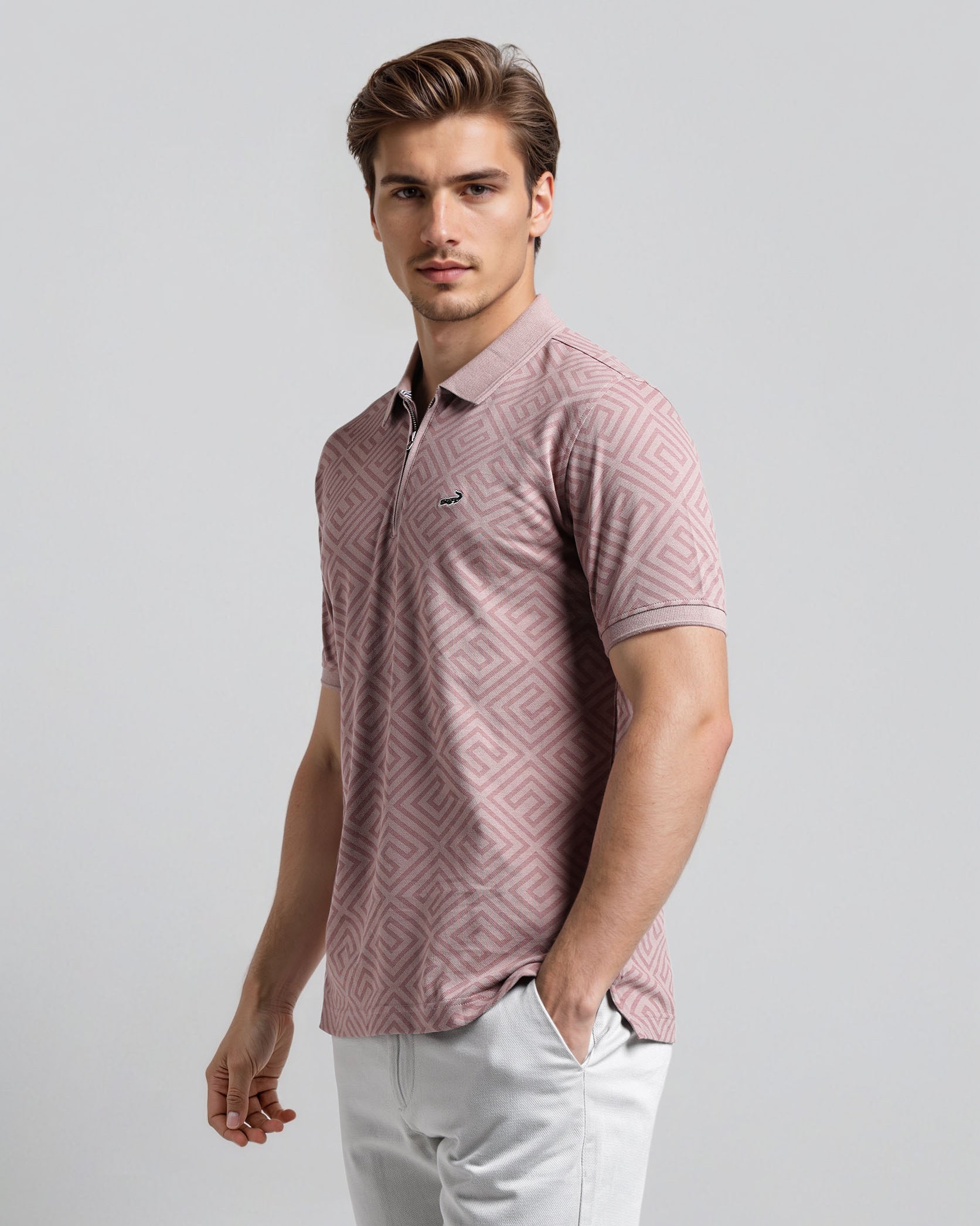 Man wearing a patterned pink shirt and light gray pants against a plain background