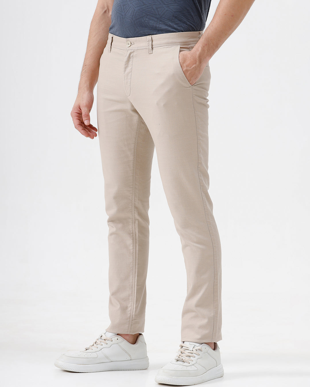 A person wearing slim-fit beige chinos with a blue patterned t-shirt and white sneakers, standing against a white studio background.