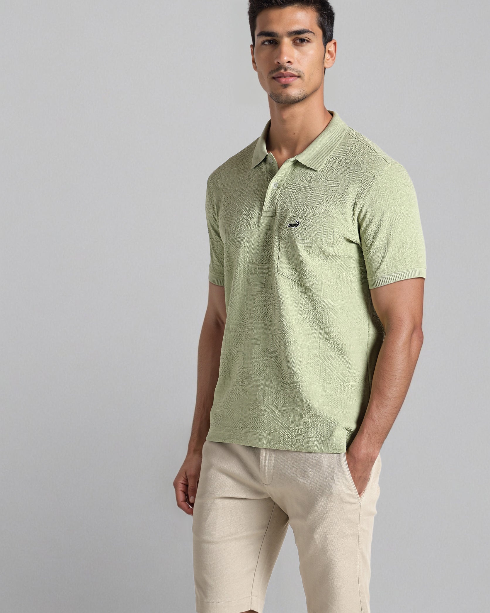 Man wearing a light green polo shirt and beige shorts on a gray background